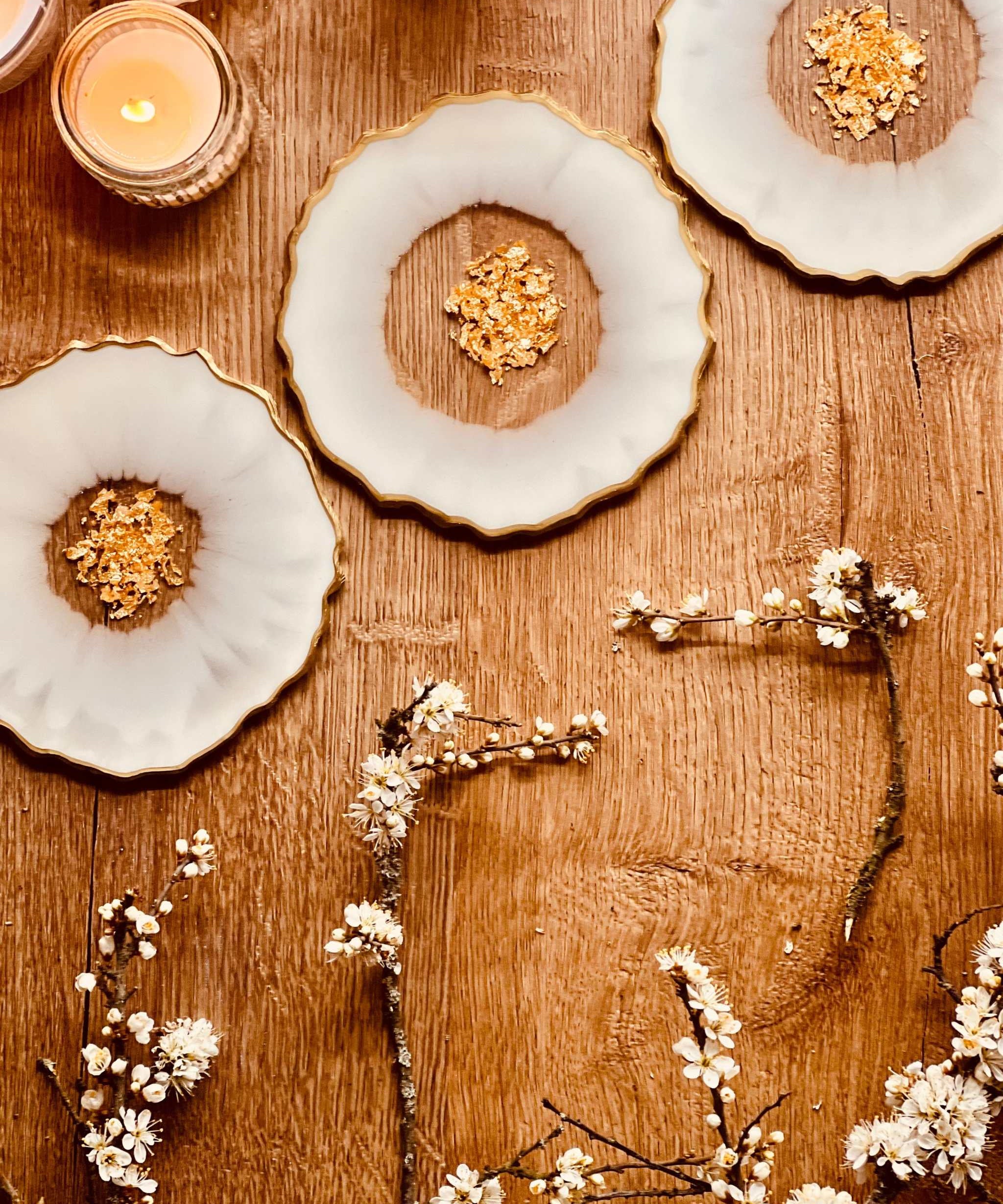 4 glitzernde Untersetzer aus Resin in Weiß mit goldenen Details auf Holztisch mit Kerzen und Blumenarrangement