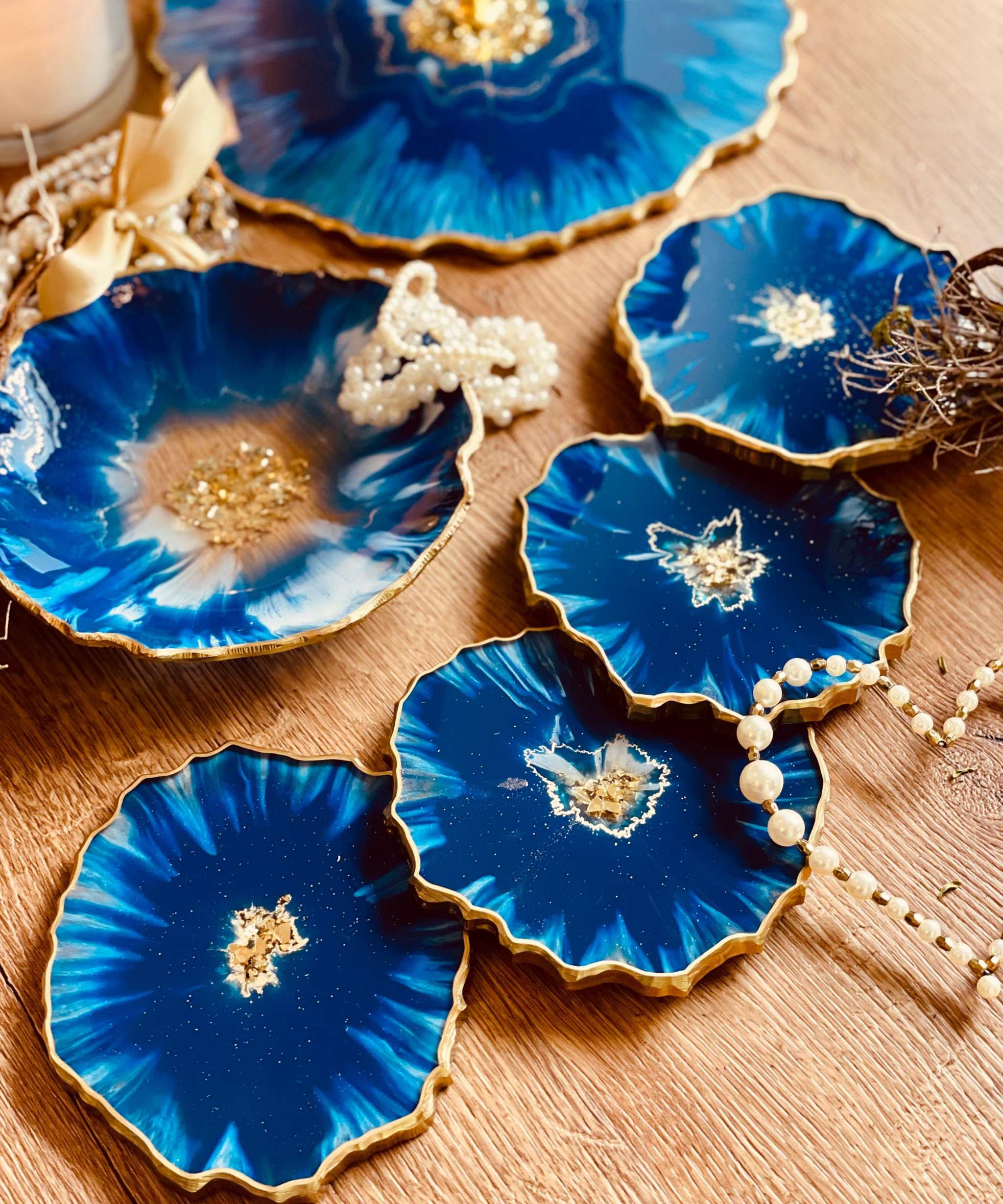 4 handgemachte blaue Resin Untersetzer mit goldenen Details und unregelmäßigen Rändern, dekorativ auf Holztisch arrangiert