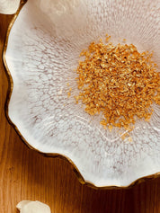 weiße handgemachte Schale aus Resin mit goldenen Dekorelementen und gewelltem Rand auf Holztisch