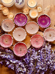 Handgemachte Schmuckschalen aus Resin in verschiedenen Pinktönen mit silbernen Details, dekorativ mit Kerzen und lila Blumen auf Holzoberfläche arrangiert