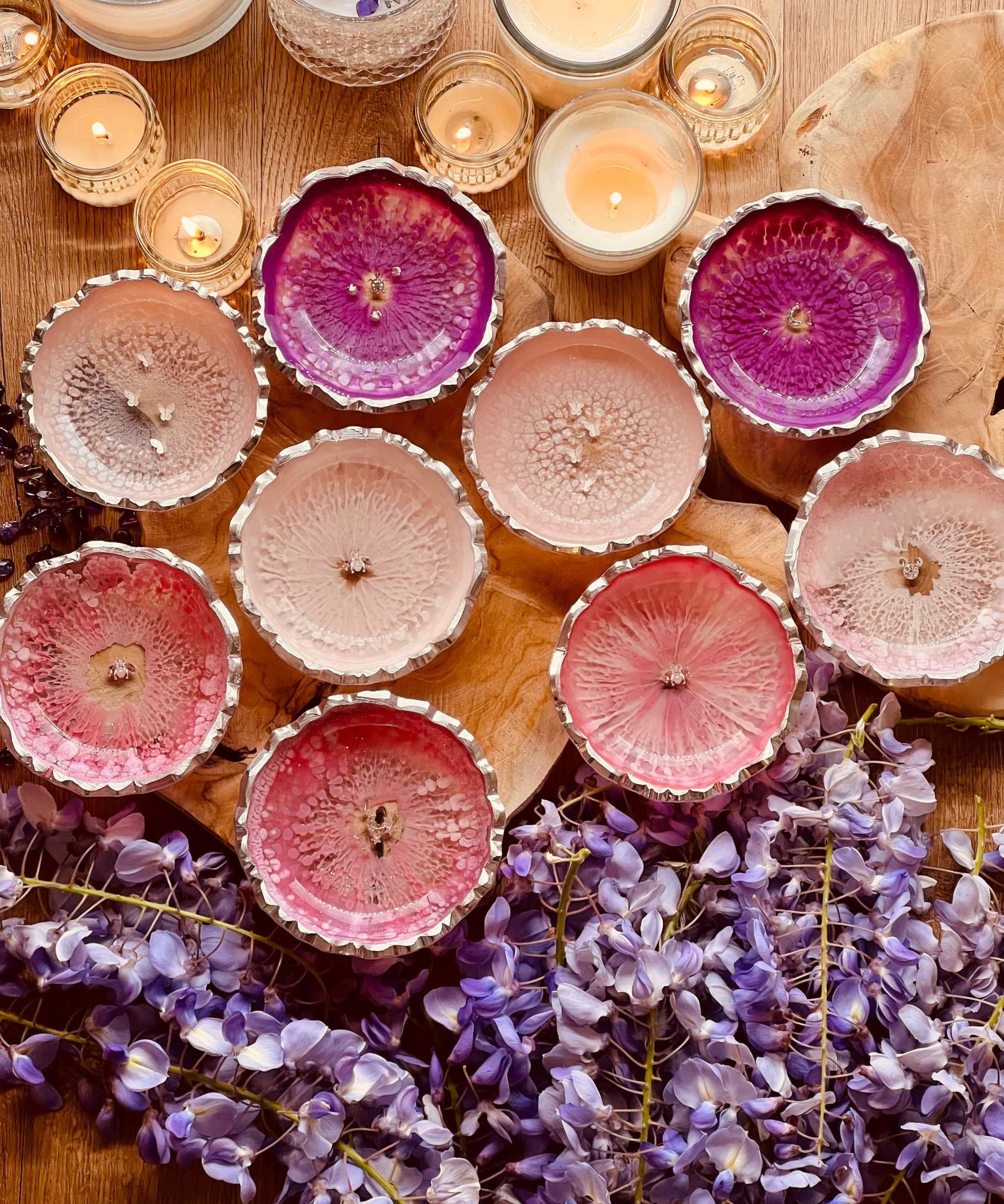 Handgemachte Schmuckschalen aus Resin in verschiedenen Pinktönen mit silbernen Details, dekorativ mit Kerzen und lila Blumen auf Holzoberfläche arrangiert