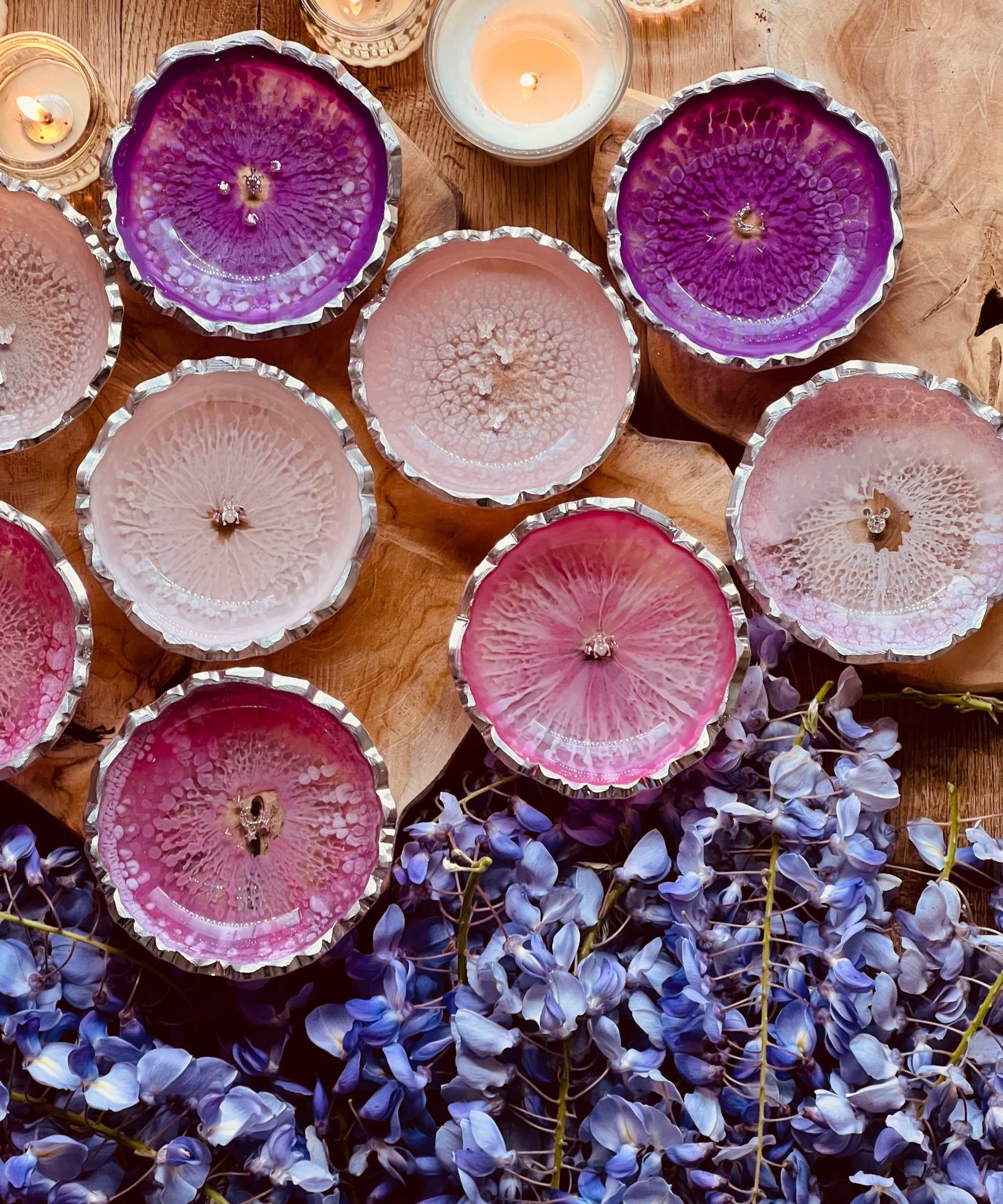 Handgemachte Schmuckschalen aus Resin in Rosa- und Pinktönen mit silbernen Details auf Holz mit Kerzen und lila Blumen dekoriert