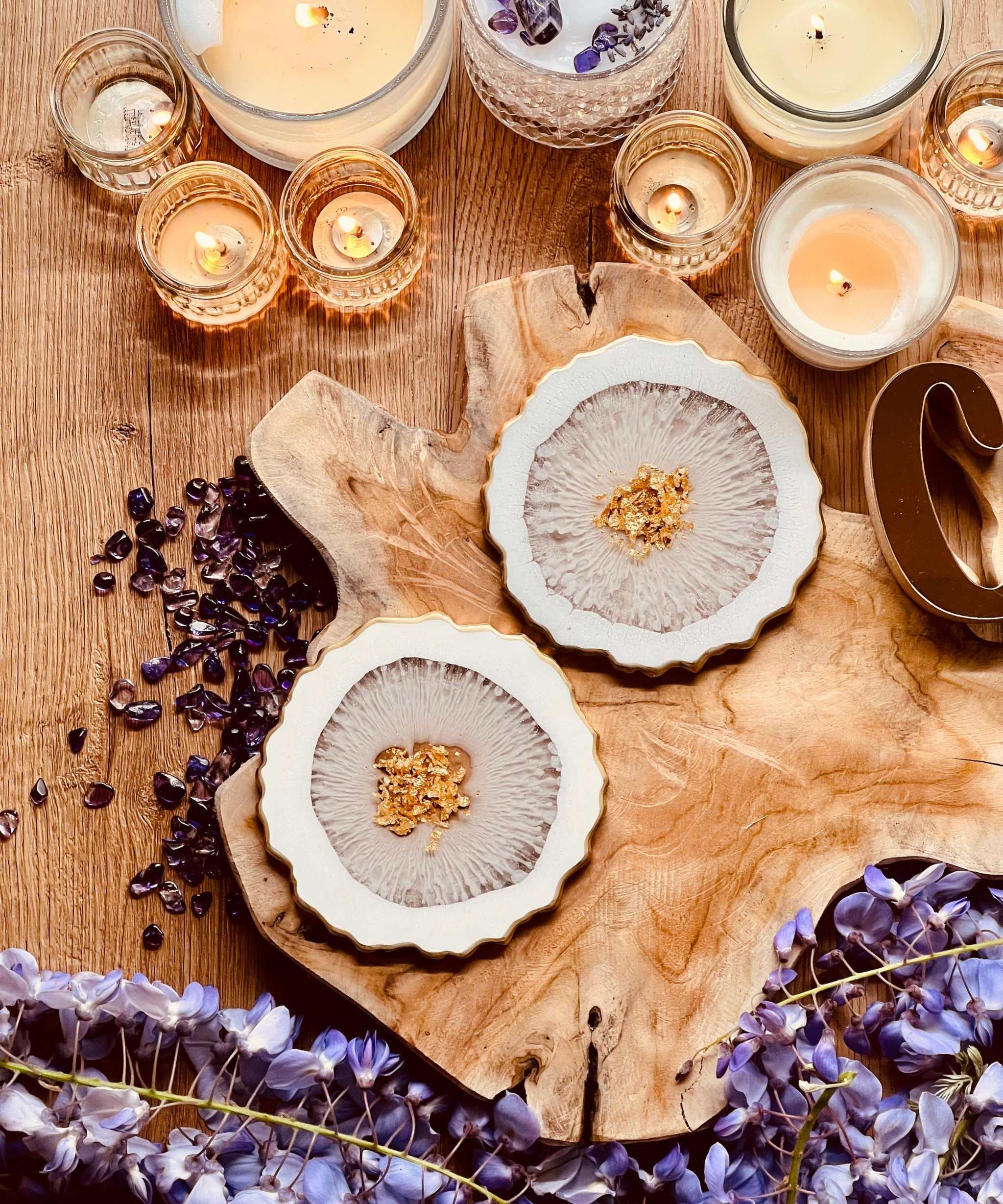 2 kunstvolle weiße Resin Untersetzer mit goldenen Details auf Holztisch zwischen Kerzen und lila Blüten
