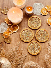 4 handgemachte goldene Untersetzer aus Resin mit diamantförmiger Oberfläche auf Holztisch mit Kerzen und getrockneten Früchten