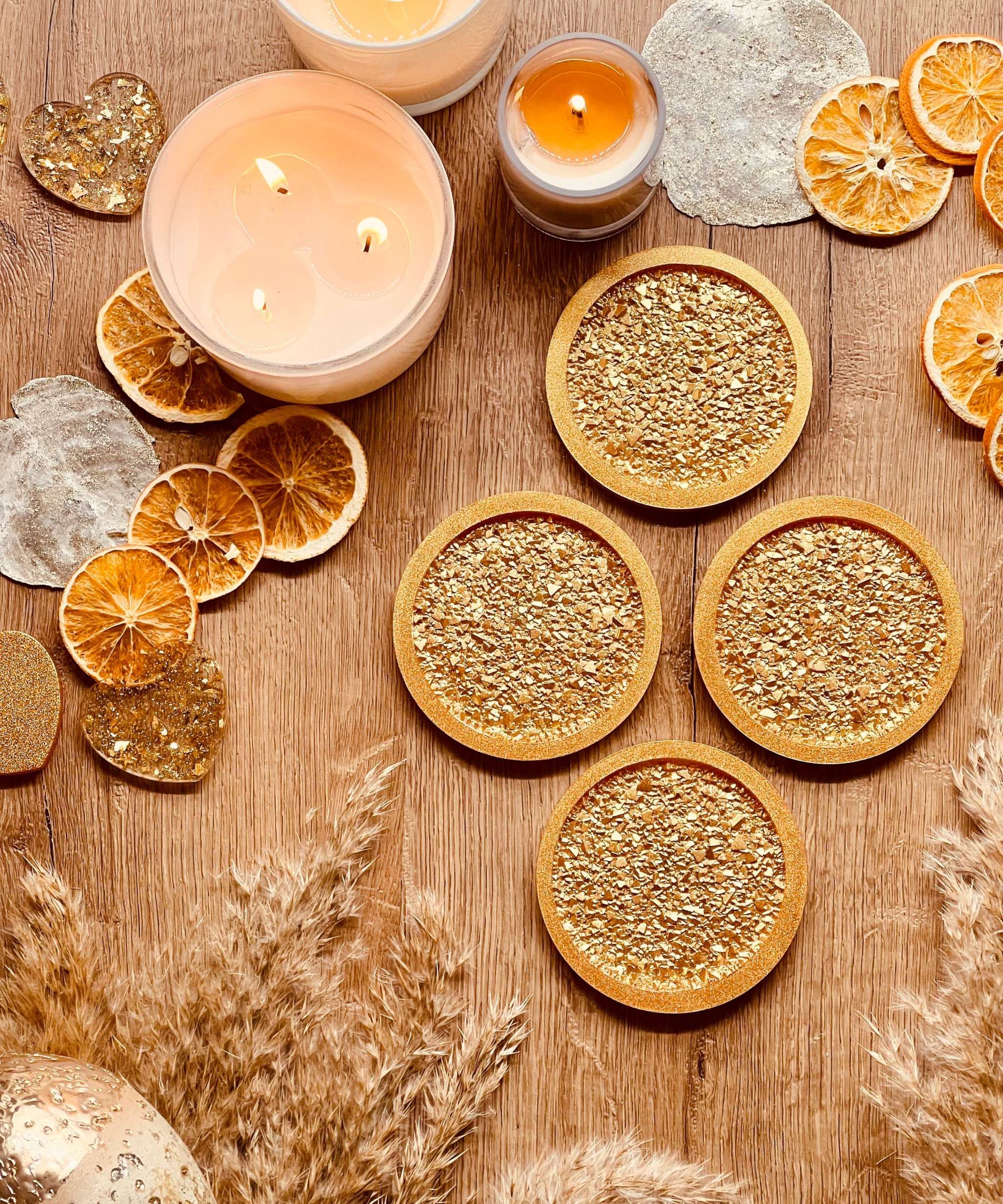 4 handgemachte goldene Untersetzer aus Resin mit diamantförmiger Oberfläche auf Holztisch mit Kerzen und getrockneten Früchten