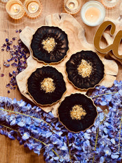 Handgemachte individuelle Untersetzer aus Resin in Schwarz mit goldenen Details, dekorativ arrangiert mit Kerzen und blauen Blüten