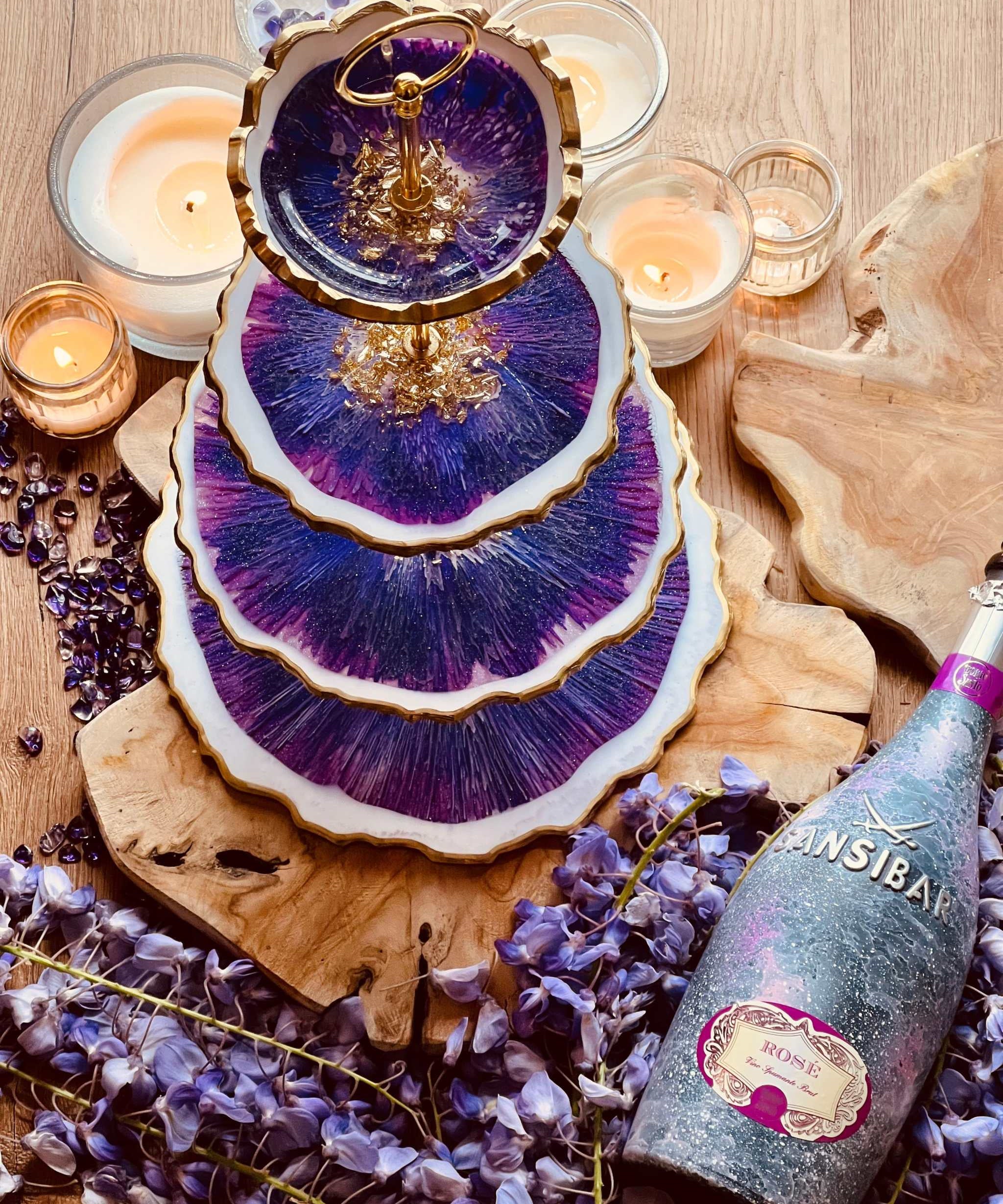 Vierstöckige Etagere aus Resin mit goldenen Akzenten und lila Marmorierung als dekoratives Unikat auf Holzplatte mit Kerzen und Rosenblüten