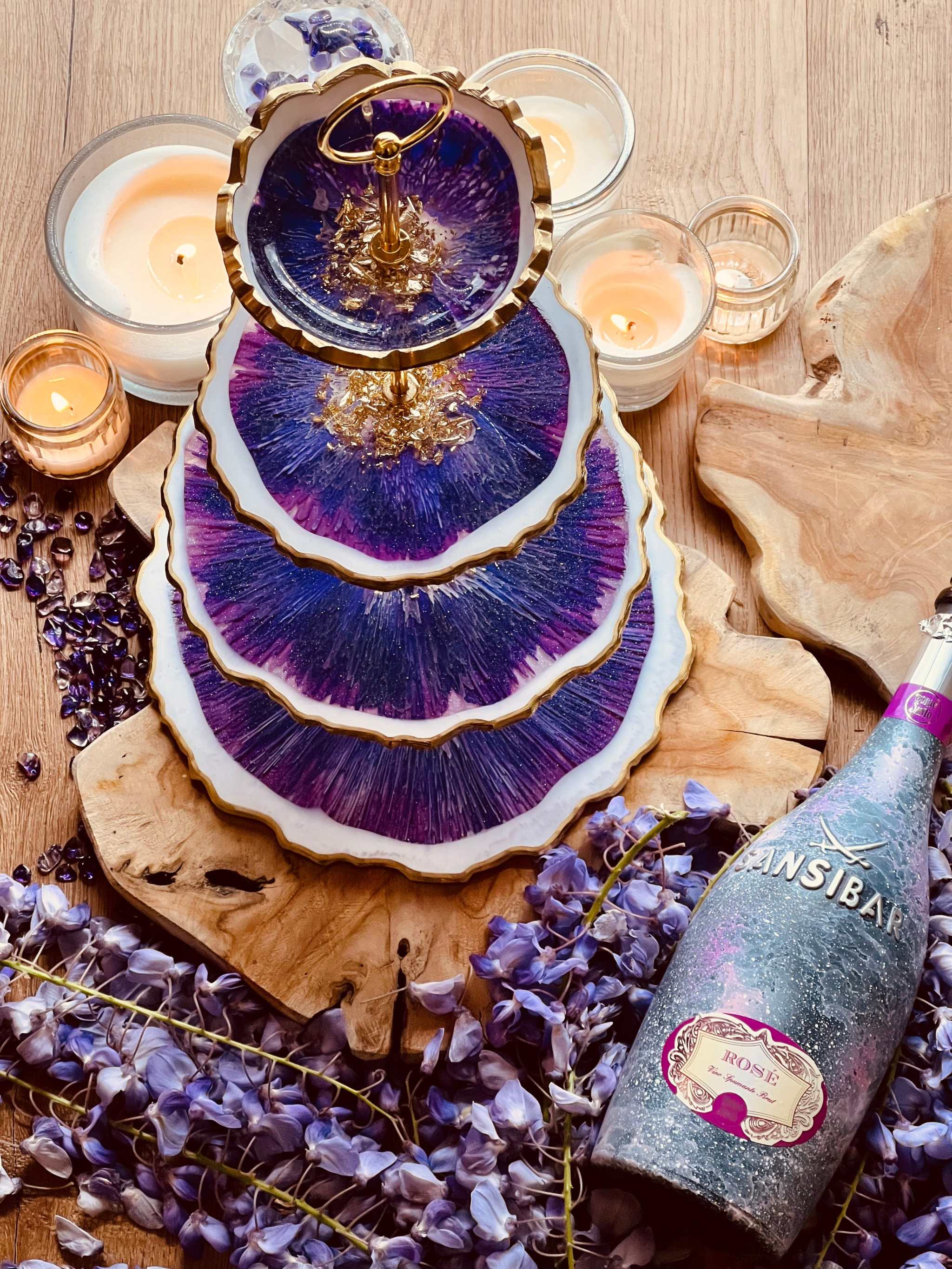 Vierstöckige Etagere aus Resin mit goldenen Akzenten und lila Marmorierung als dekoratives Unikat auf Holzplatte mit Kerzen und Rosenblüten