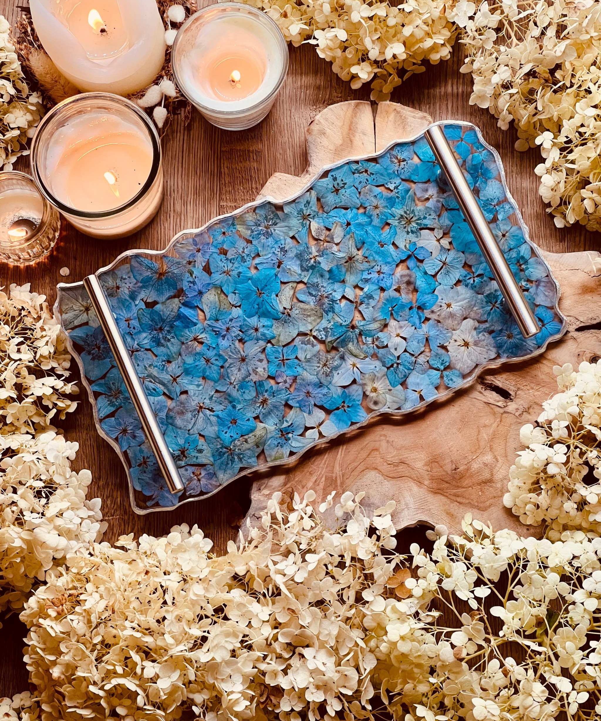 Handgemachtes Resin Tablett mit blauen Hortensien und silbernen Griffen auf Holzuntergrund mit Kerzen und Trockenblumen