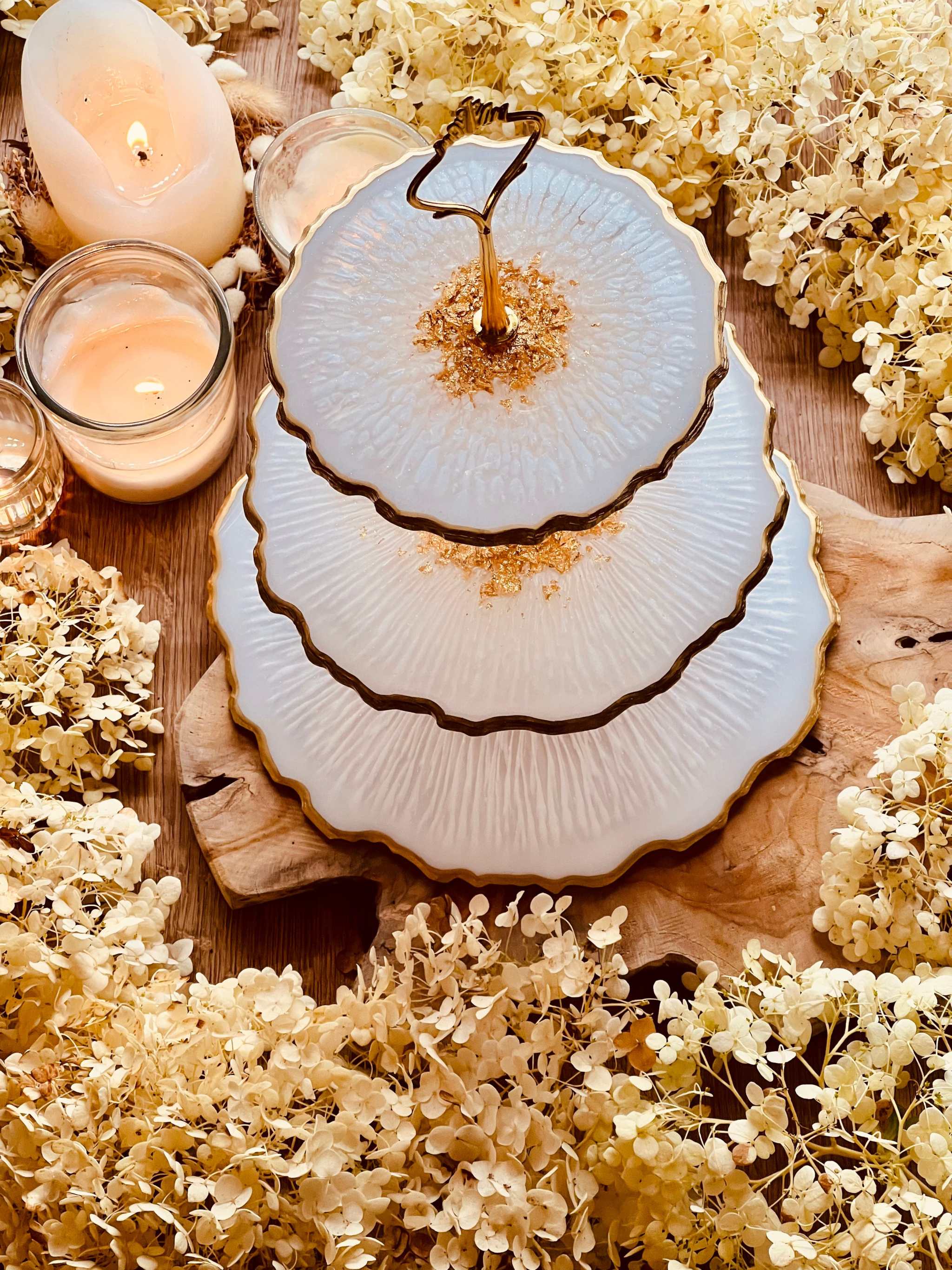 dreistöckige edle resin etagere mit goldrand handgemacht auf holzplatte umgeben von getrockneten blumen und kerzen