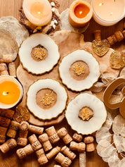 4 glitzernde handgemachte Untersetzer aus weißem Resin mit goldenen Details im 4er Set auf Holztisch mit Kerzen und Korken