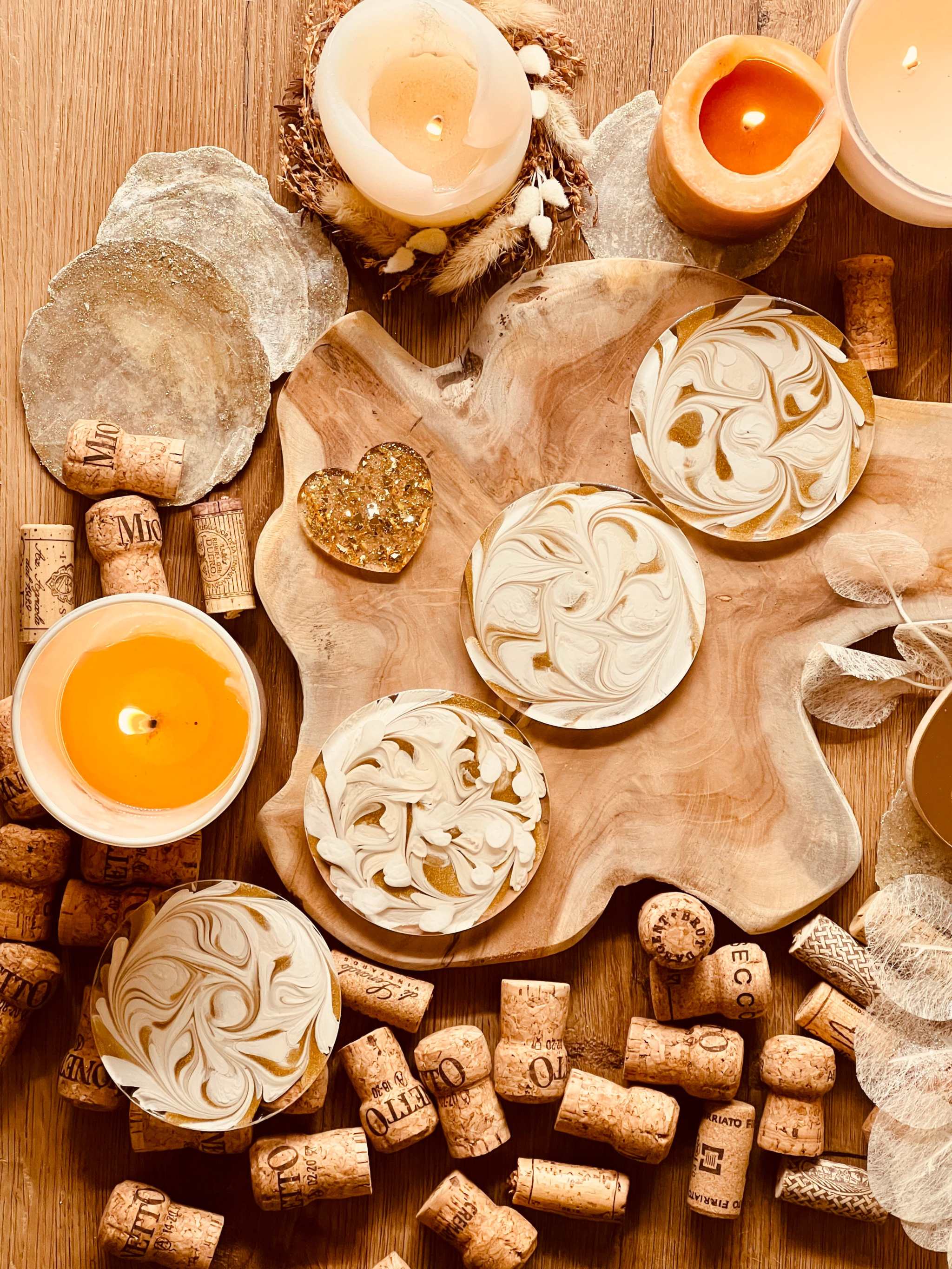 4 künstlerische Untersetzer aus weißem Resin mit goldenen Details auf Holztisch mit Kerzen und Weinkorken