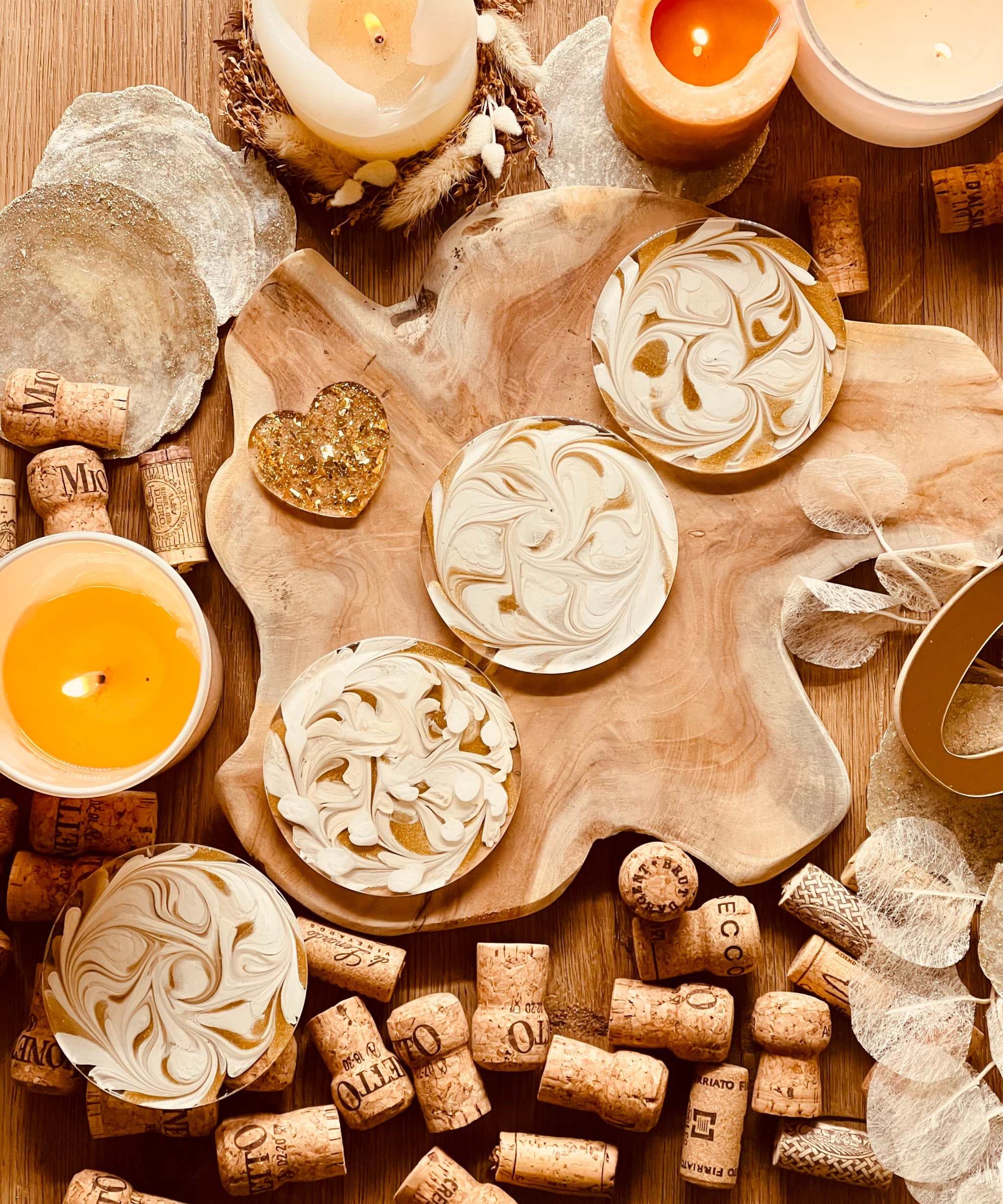4 handgemachte künstlerische Untersetzer aus weißem Resin mit goldenen Details auf einem Holztablett zwischen Kerzen und Korken