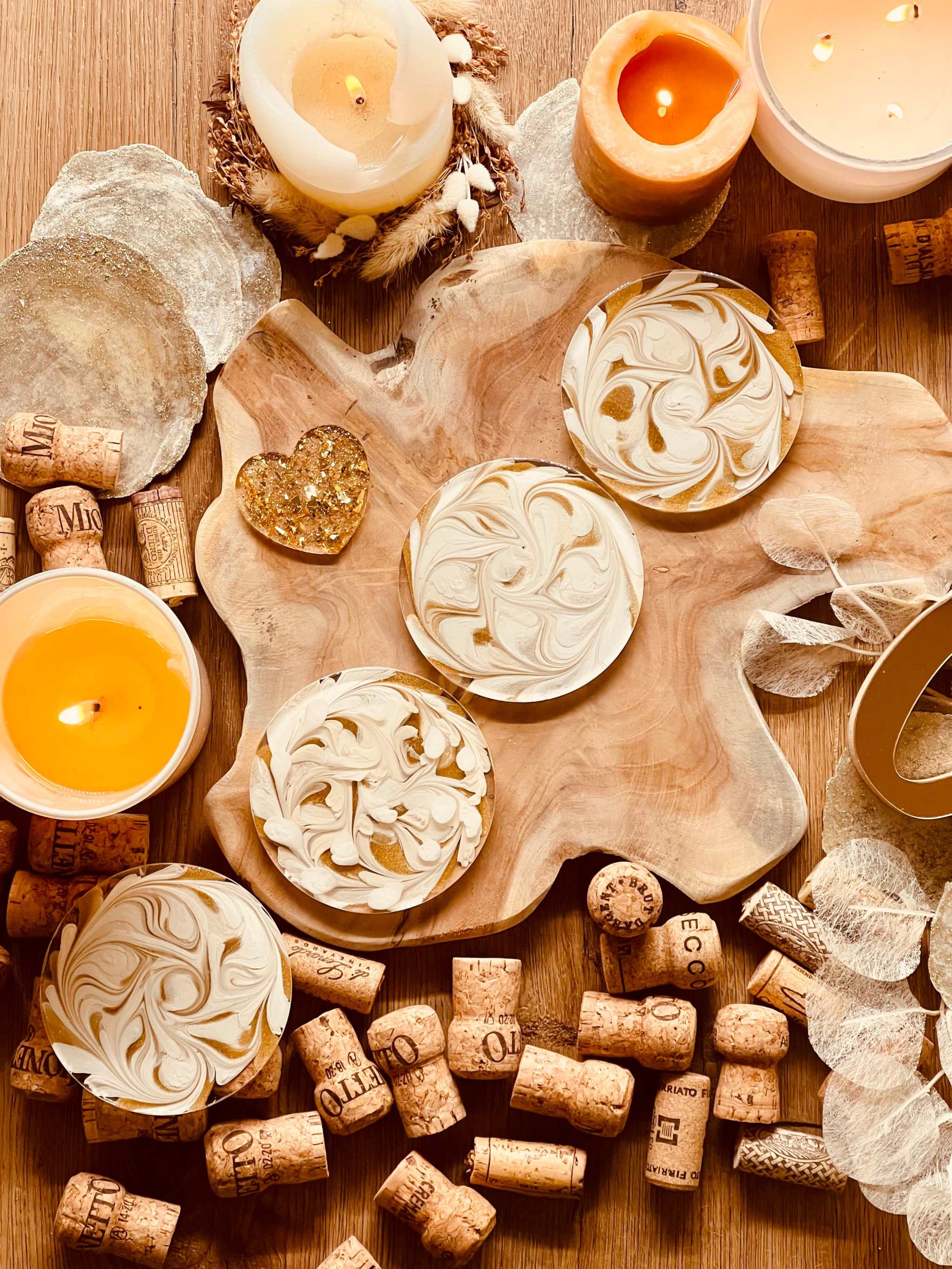 4 handgemachte künstlerische Untersetzer aus weißem Resin mit goldenen Details auf einem Holztablett zwischen Kerzen und Korken