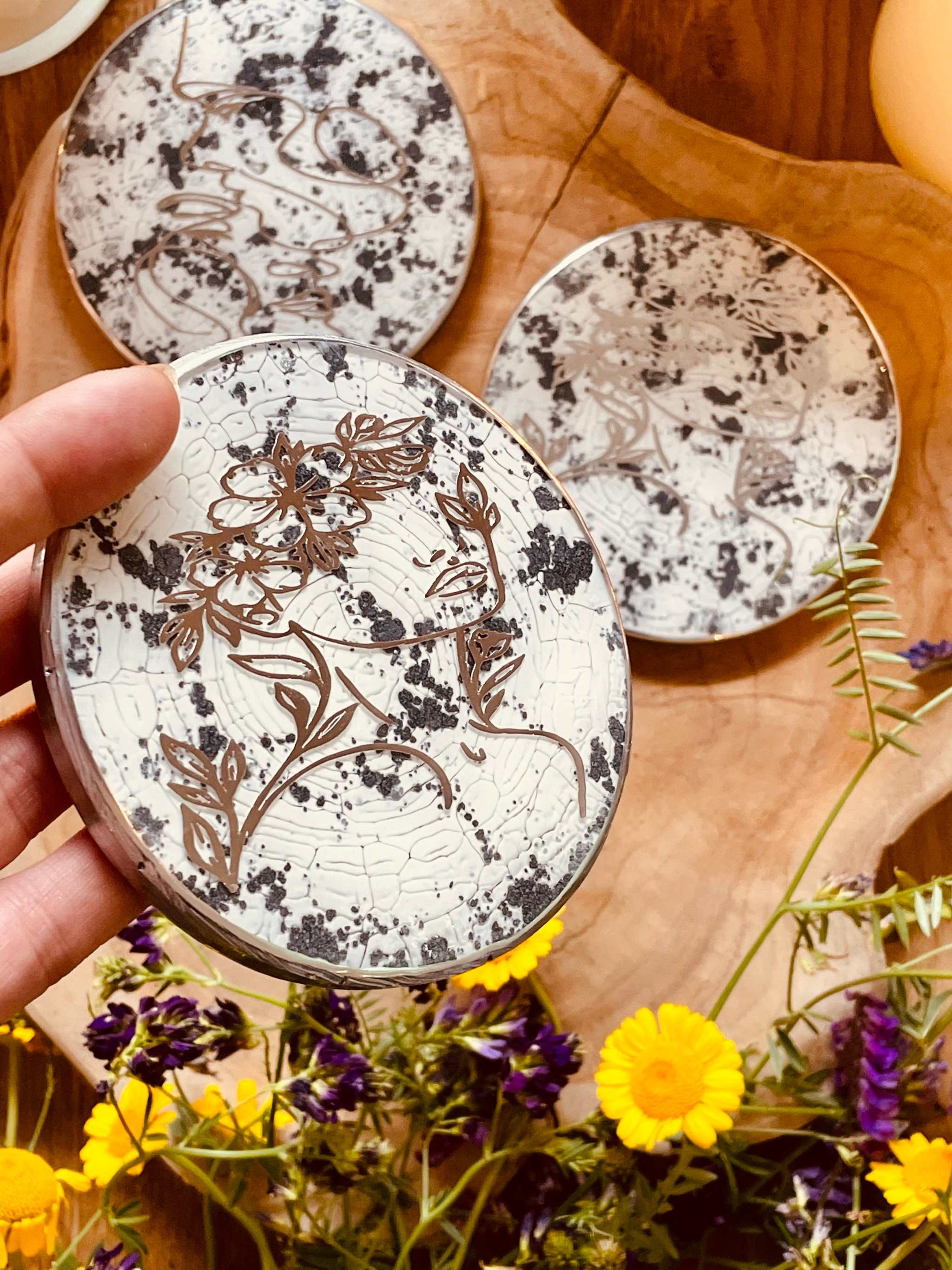 3 Untersetzer aus Resin in Schwarz-Weiß-Silber mit floralem LineArt-Muster auf Holztisch mit Blumenarrangement