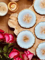 6 handgemachte weiße Resin-Untersetzer mit goldenen Details auf Holztisch mit Kerzen und Rosen
