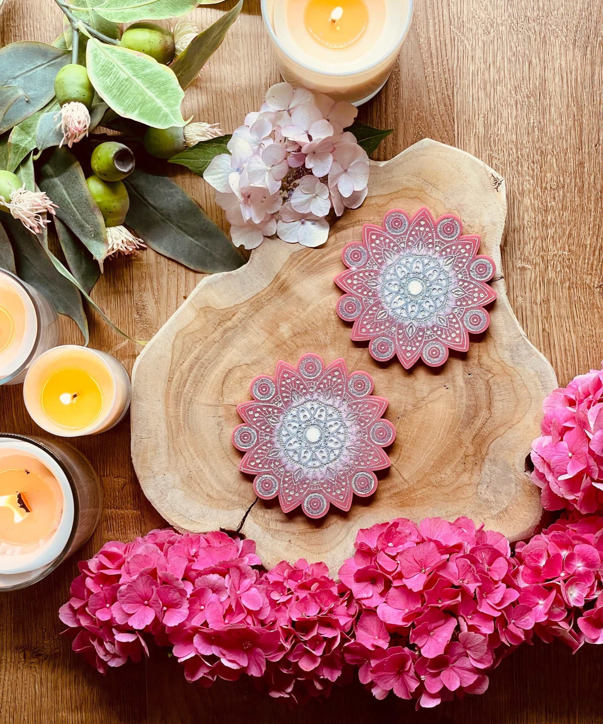 2 handgemachte Mandala Untersetzer aus Resin in Pink mit silbernen Details auf Holzplatte mit Blumen und Kerzen dekoriert