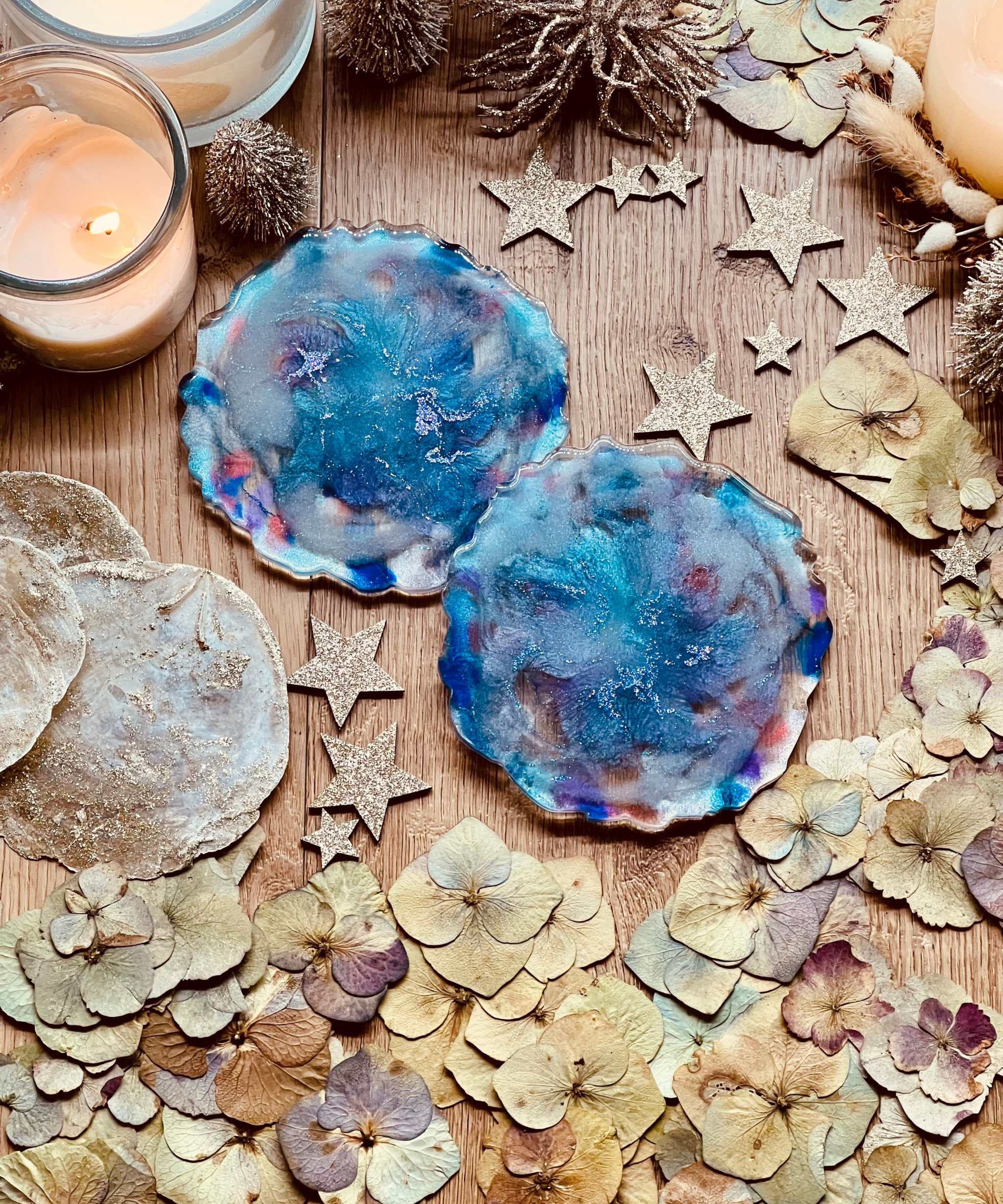 2 handgemachte Untersetzer aus Resin in Blautönen als 2-teiliges Set auf dekorativem Holztisch mit Kerzen und getrockneten Blüten