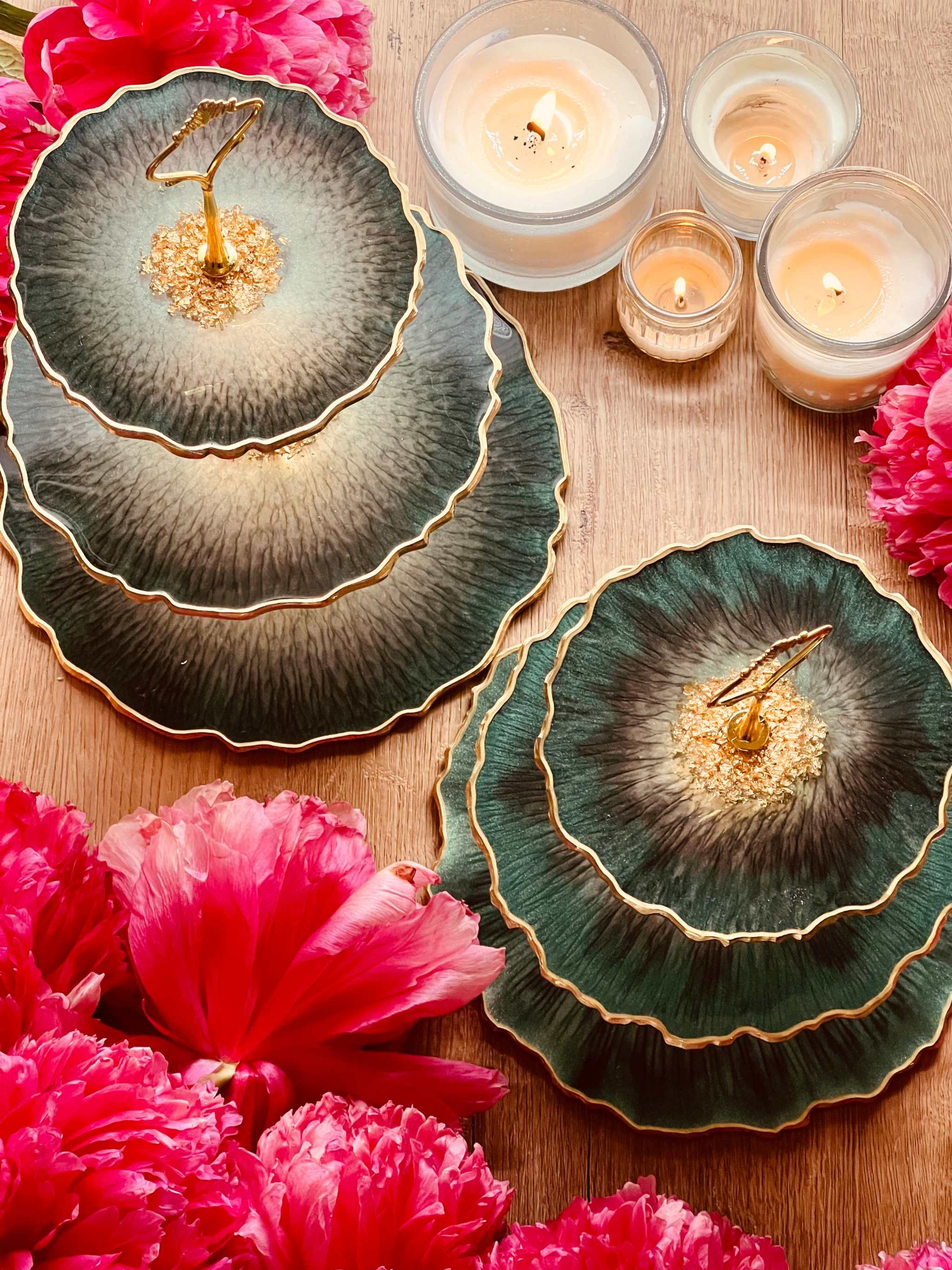 dreistöckige handgemachte resin etagere in unregelmäßiger, geschwungener form mit goldenen kanten auf holztisch mit kerzen und rosa blüten