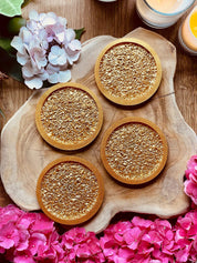 4 goldene Untersetzer aus Resin mit diamantförmiger Oberfläche auf Holztablett, dekoriert mit Blumen und Kerzen
