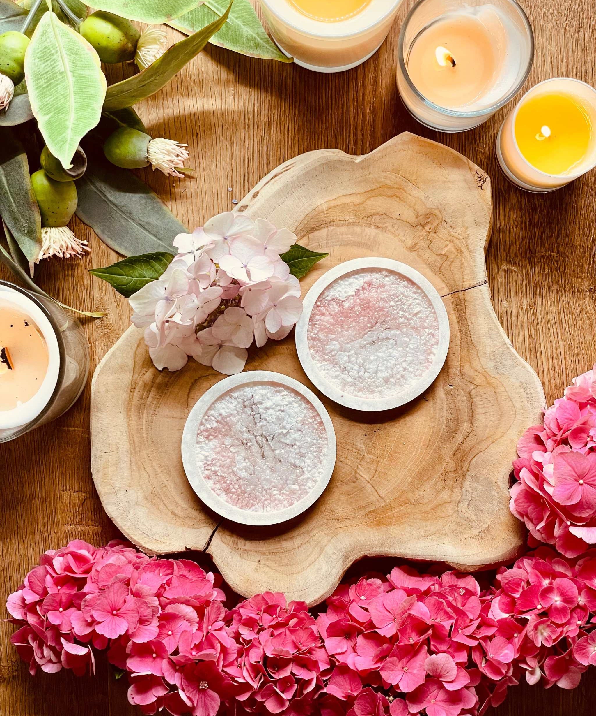 Zwei handgemachte rosa Untersetzer aus Resin mit Diamantoberfläche auf Holzplatte dekoriert mit Blumen und Kerzen