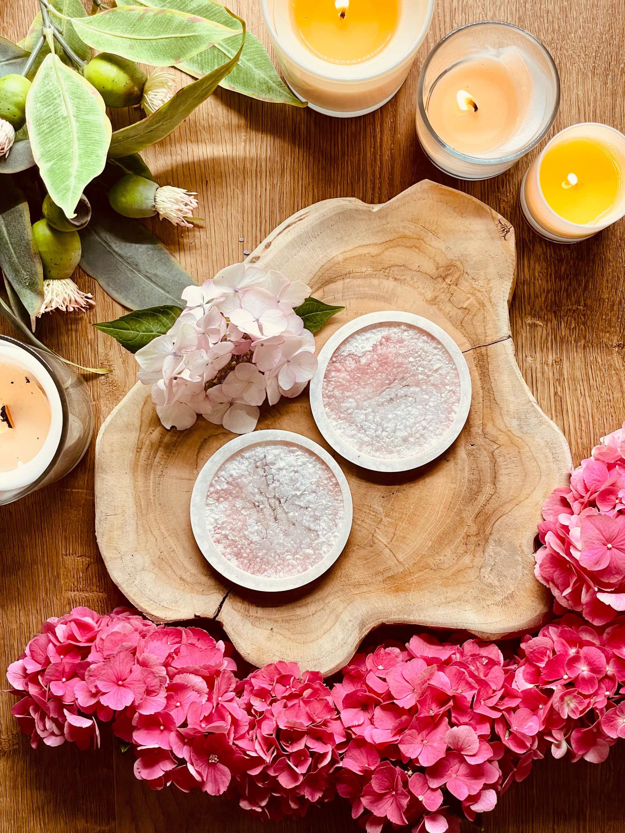Zwei handgemachte rosa Untersetzer aus Resin mit Diamantoberfläche auf Holzplatte dekoriert mit Blumen und Kerzen