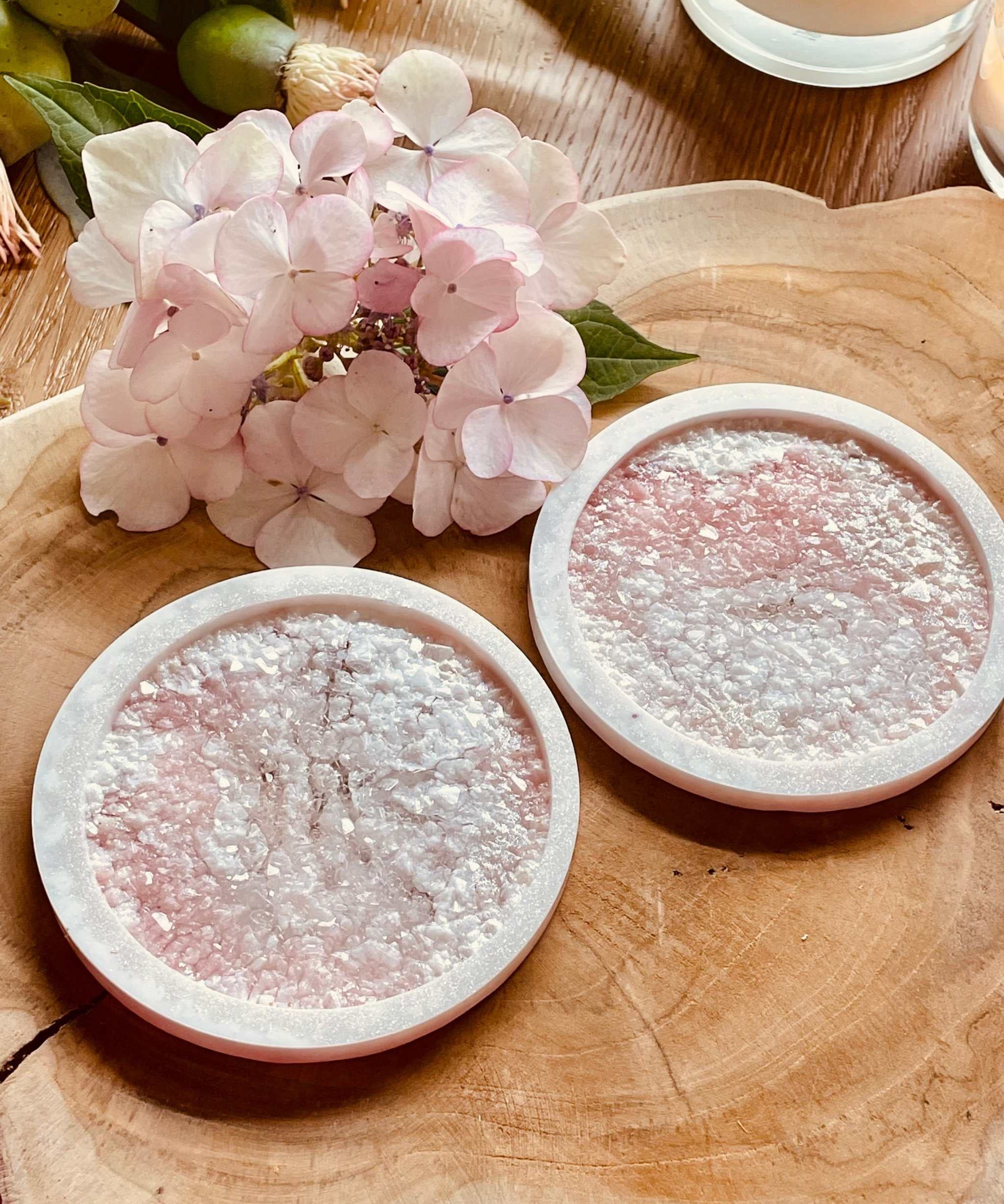 Zwei handgemachte rosa Untersetzer aus Resin mit diamantstrukturierter Oberfläche auf Holztisch mit rosa Blüten