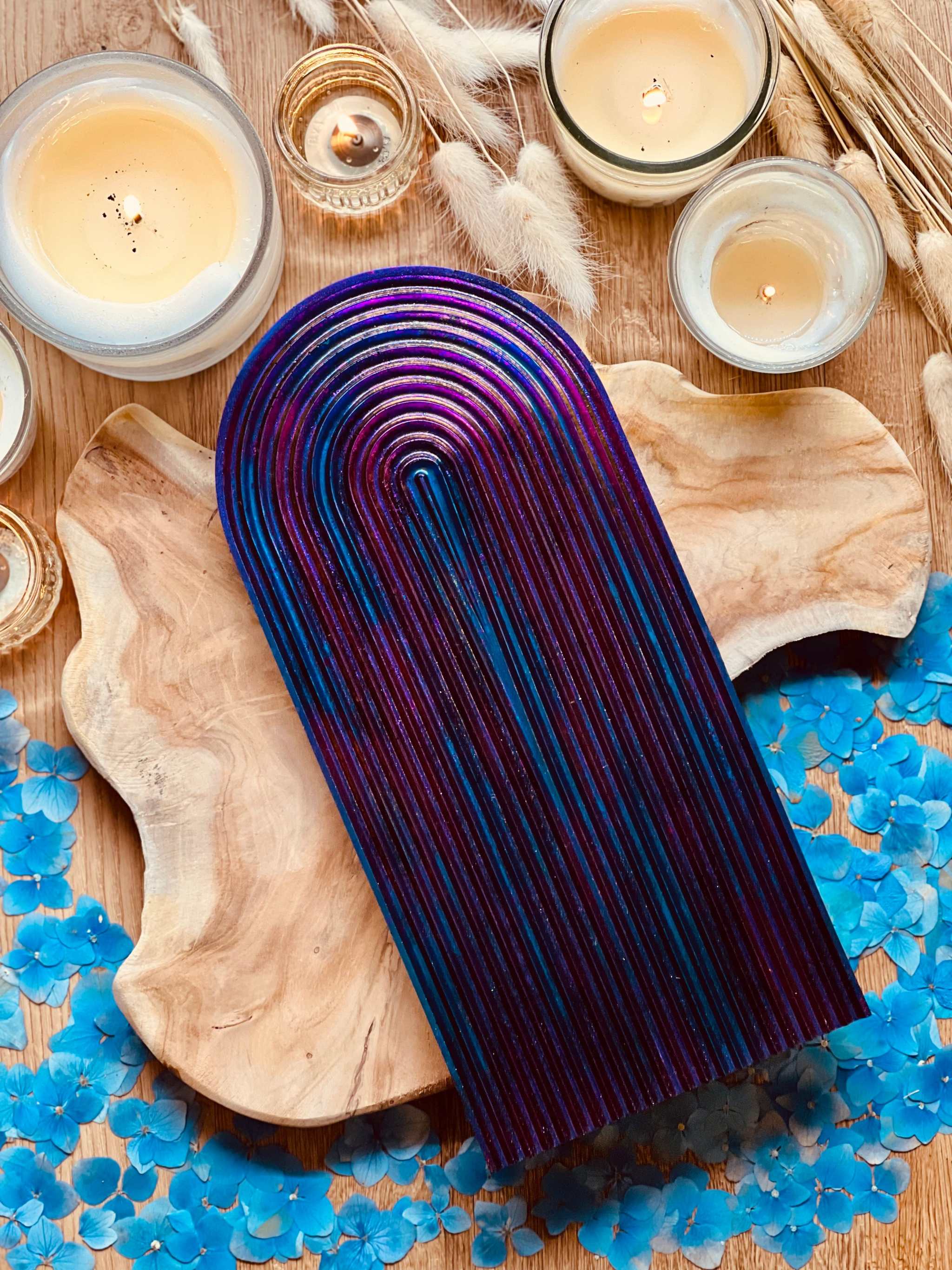 Handgemachtes Rainbow Tablett aus Resin mit Regenbogen Design in Chameleon Farben, einzigartige Deko auf Holzunterlage, umgeben von Kerzen und blauen Blüten