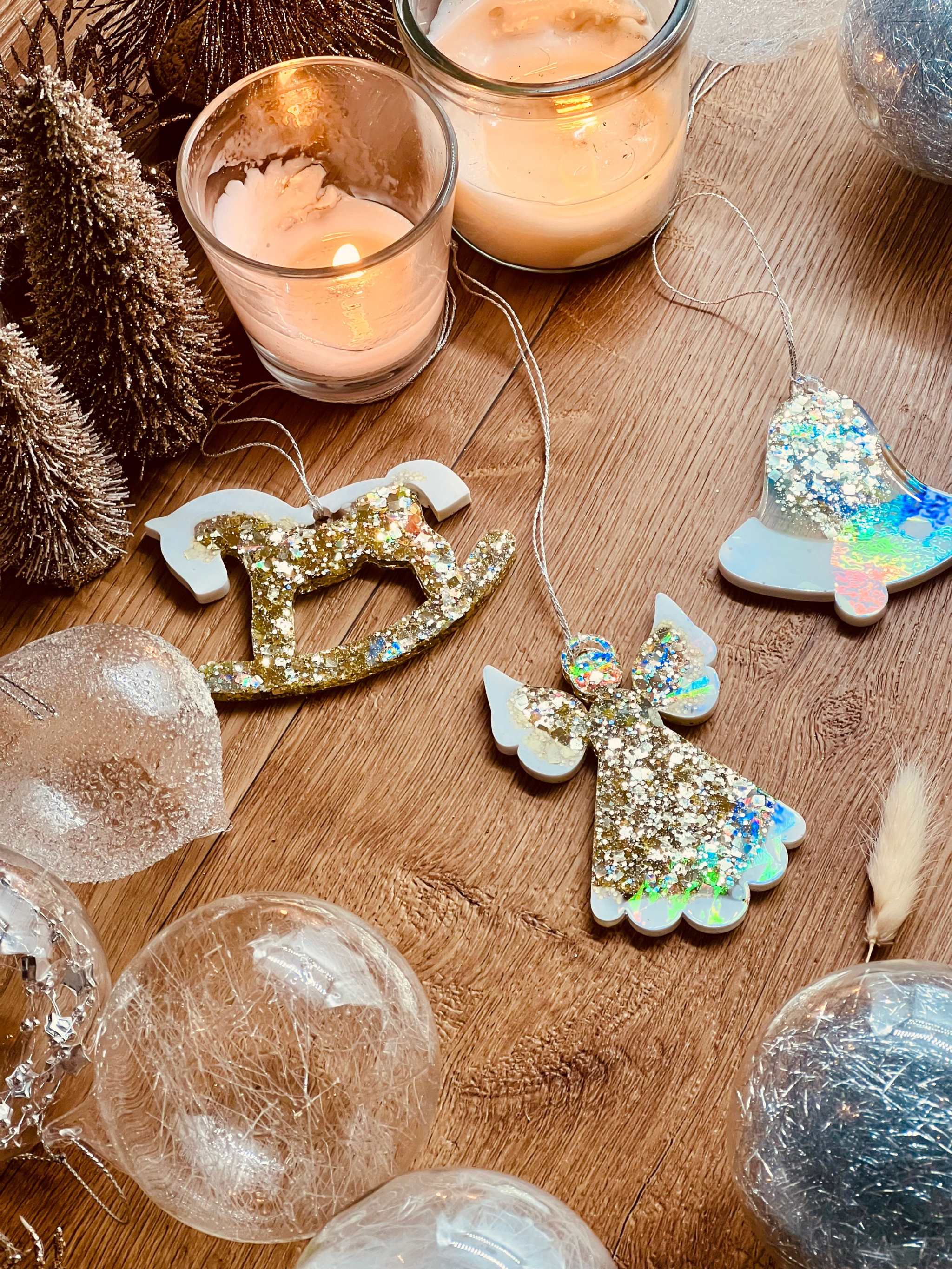 3 handgemachte Weihnachtsbaumanhänger aus Resin in Gold und Weiß mit holographischer Oberfläche, liegend auf einem Tisch.