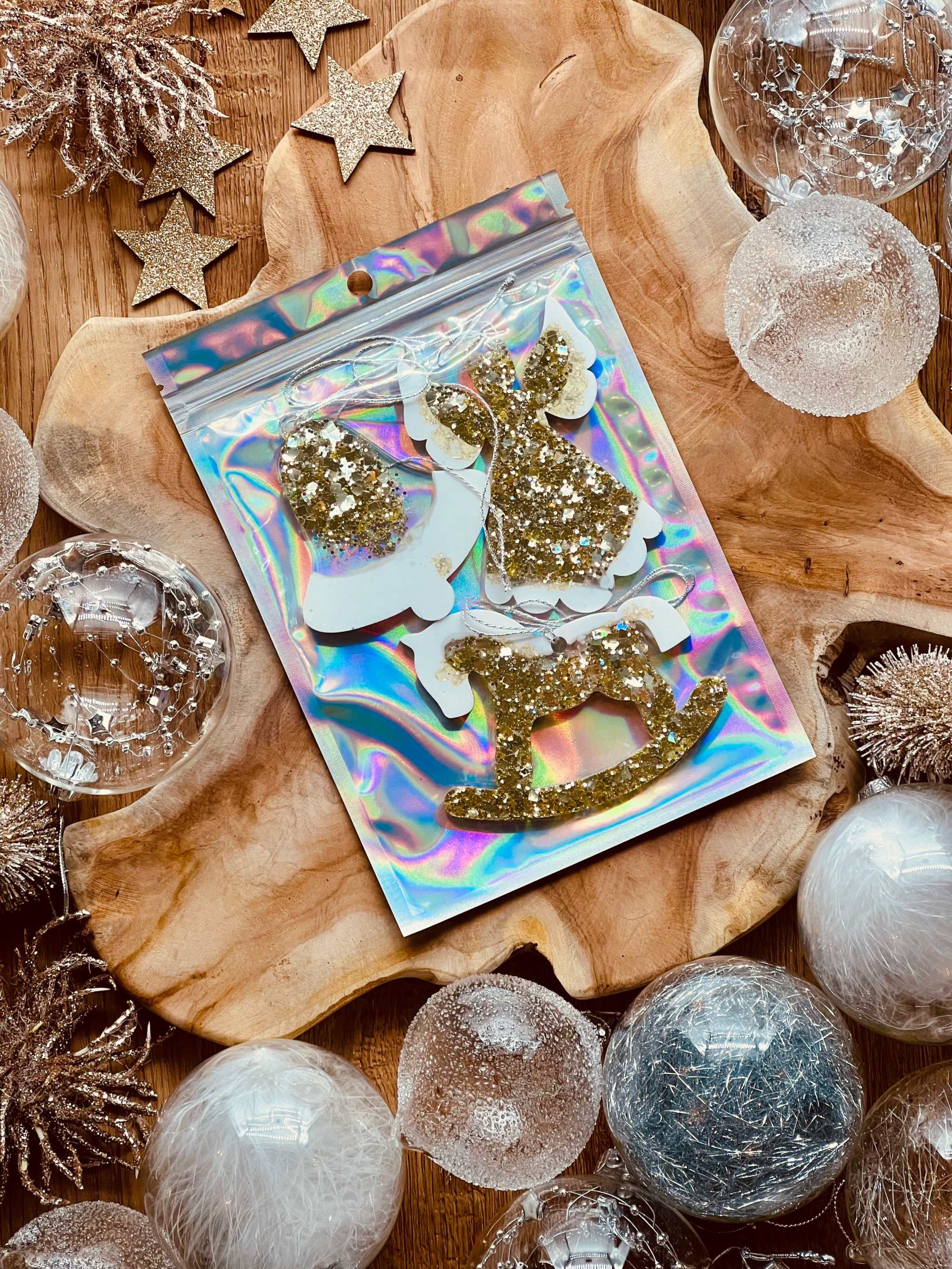Gold and white resin Christmas tree ornaments with holographic surface on wooden background.