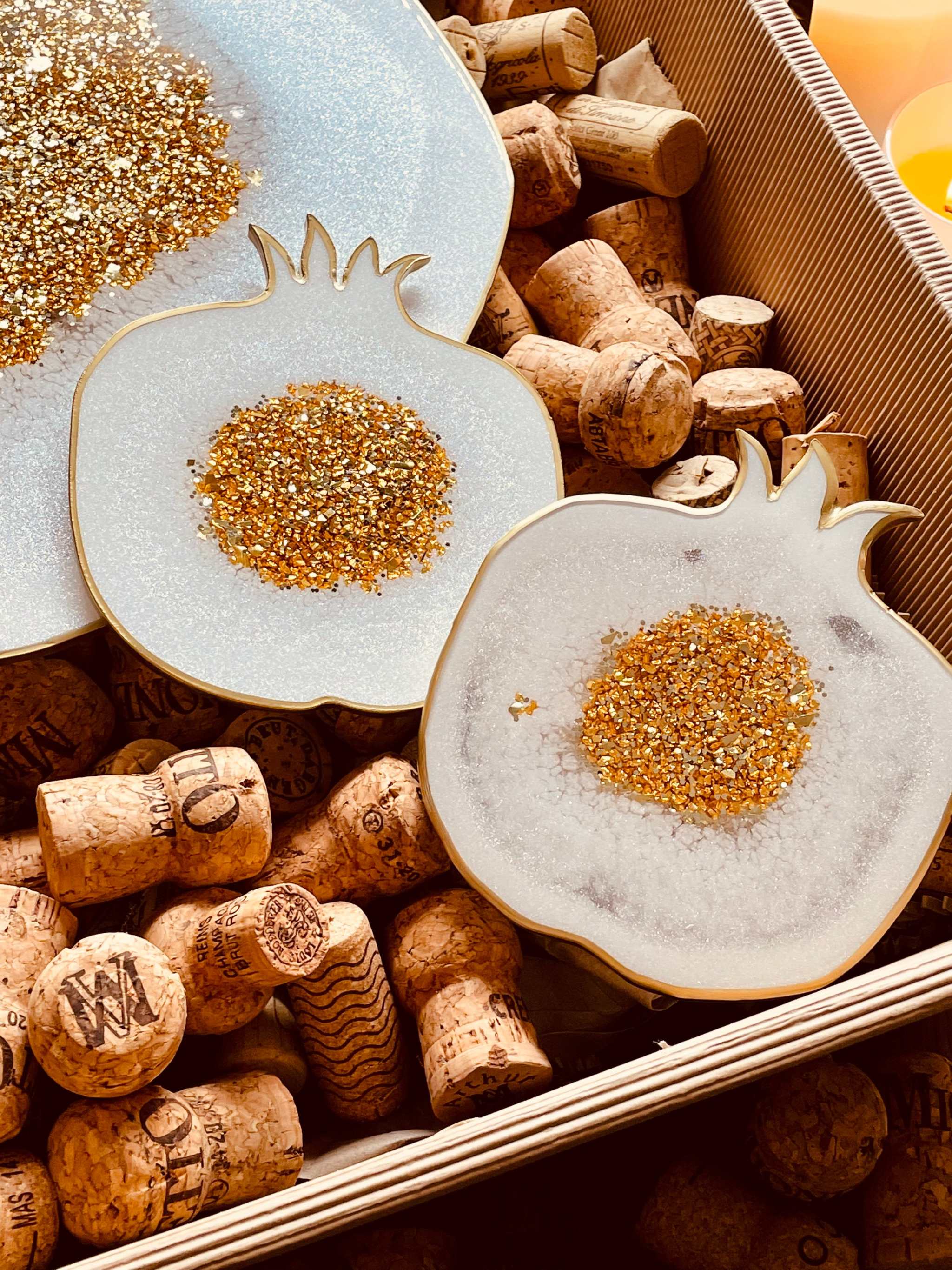 weißes handgemachtes Resin Tablett und zwei Untersetzer mit goldenen Granatapfel-Designs auf Korken in Holzkiste