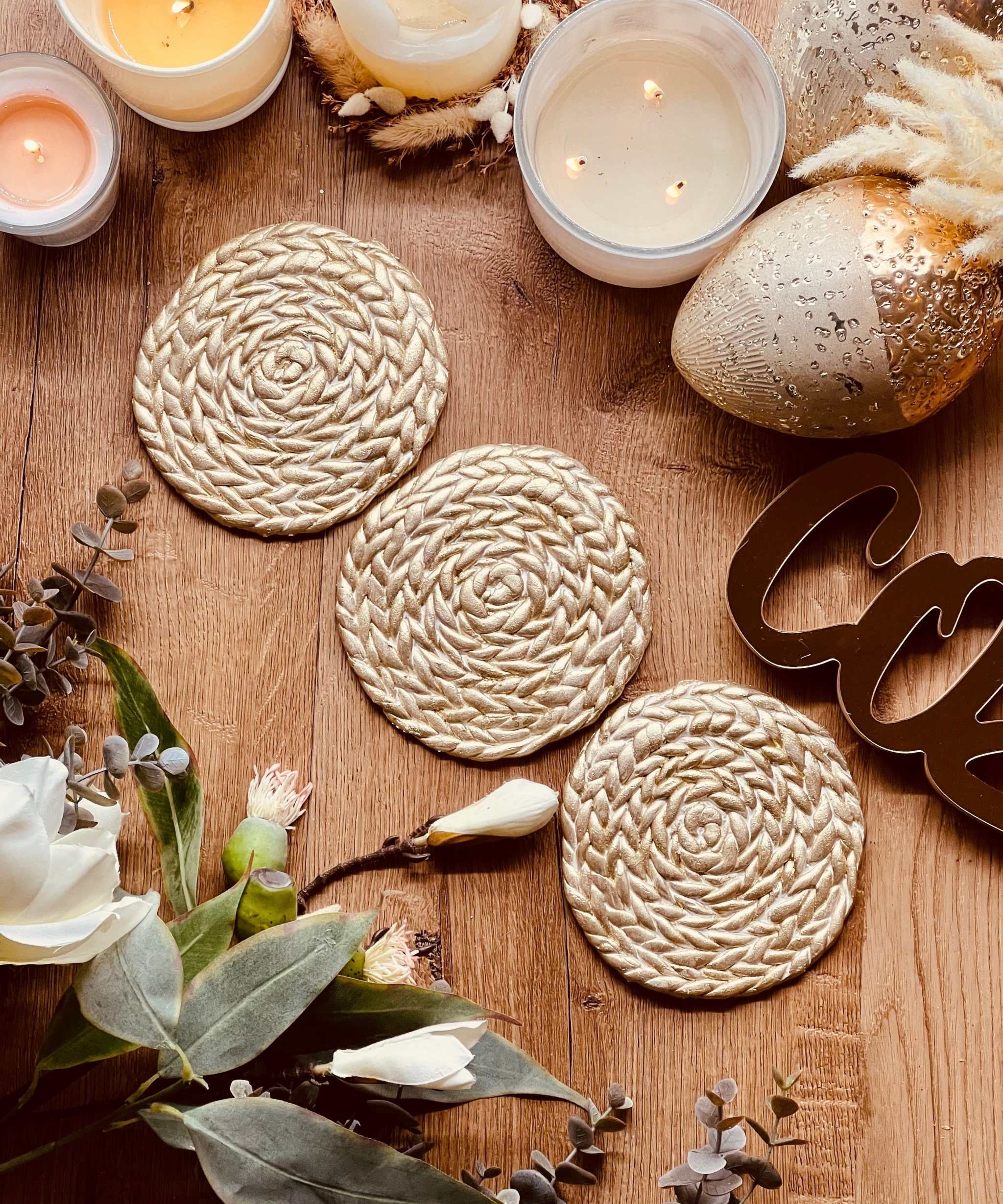 Handgemachte goldene Untersetzer aus Clay mit spiralförmigem Muster auf Holztisch mit Kerzen und Dekorationen