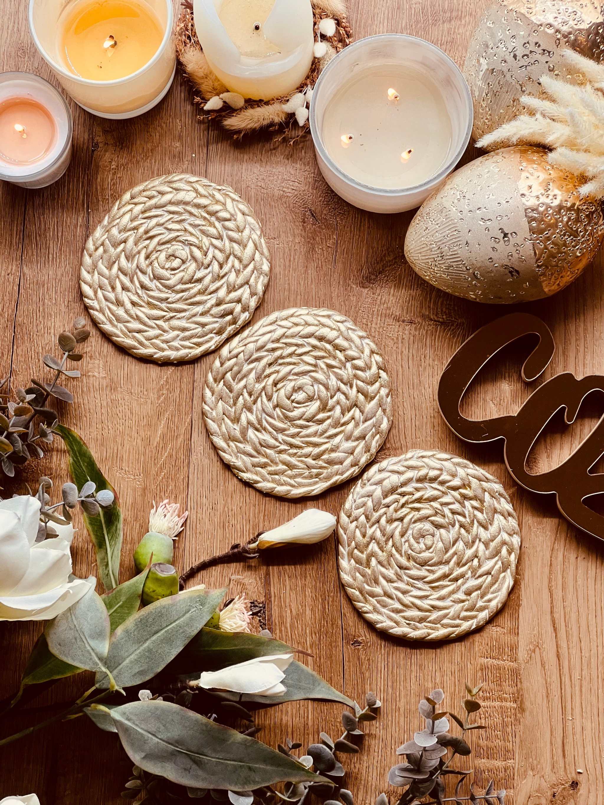 Handgemachte goldene Untersetzer aus Clay mit spiralförmigem Muster auf Holztisch mit Kerzen und Dekorationen