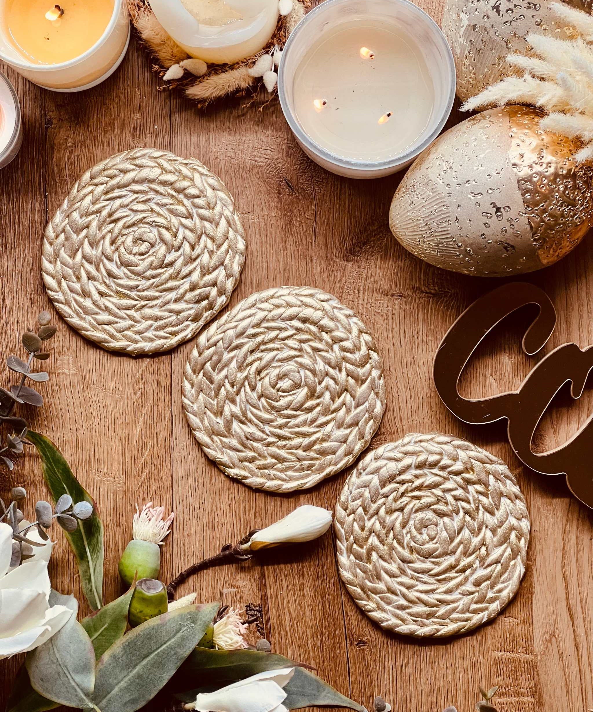 handgemachte goldene untersetzer aus clay mit geflochtenem muster und kerzen dekor auf holztisch