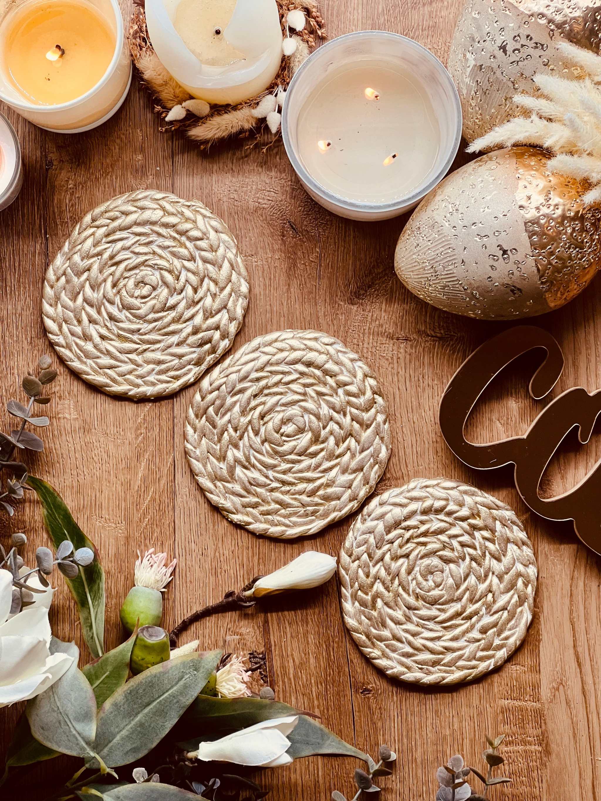 handgemachte goldene untersetzer aus clay mit geflochtenem muster und kerzen dekor auf holztisch