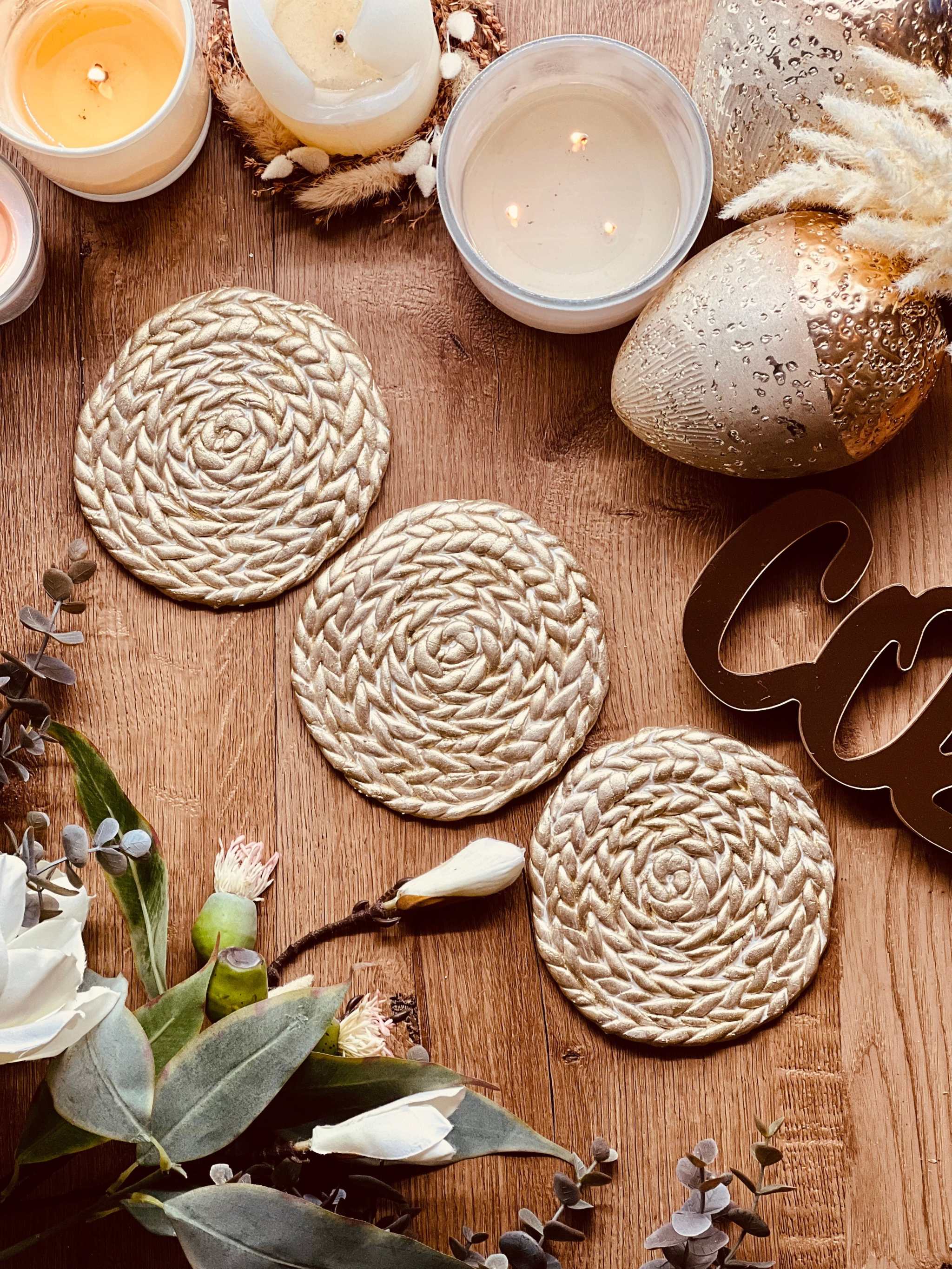 Handgemachte goldene Untersetzer aus Clay mit geflochtenem Design auf Holztisch mit Kerzen und Dekoration