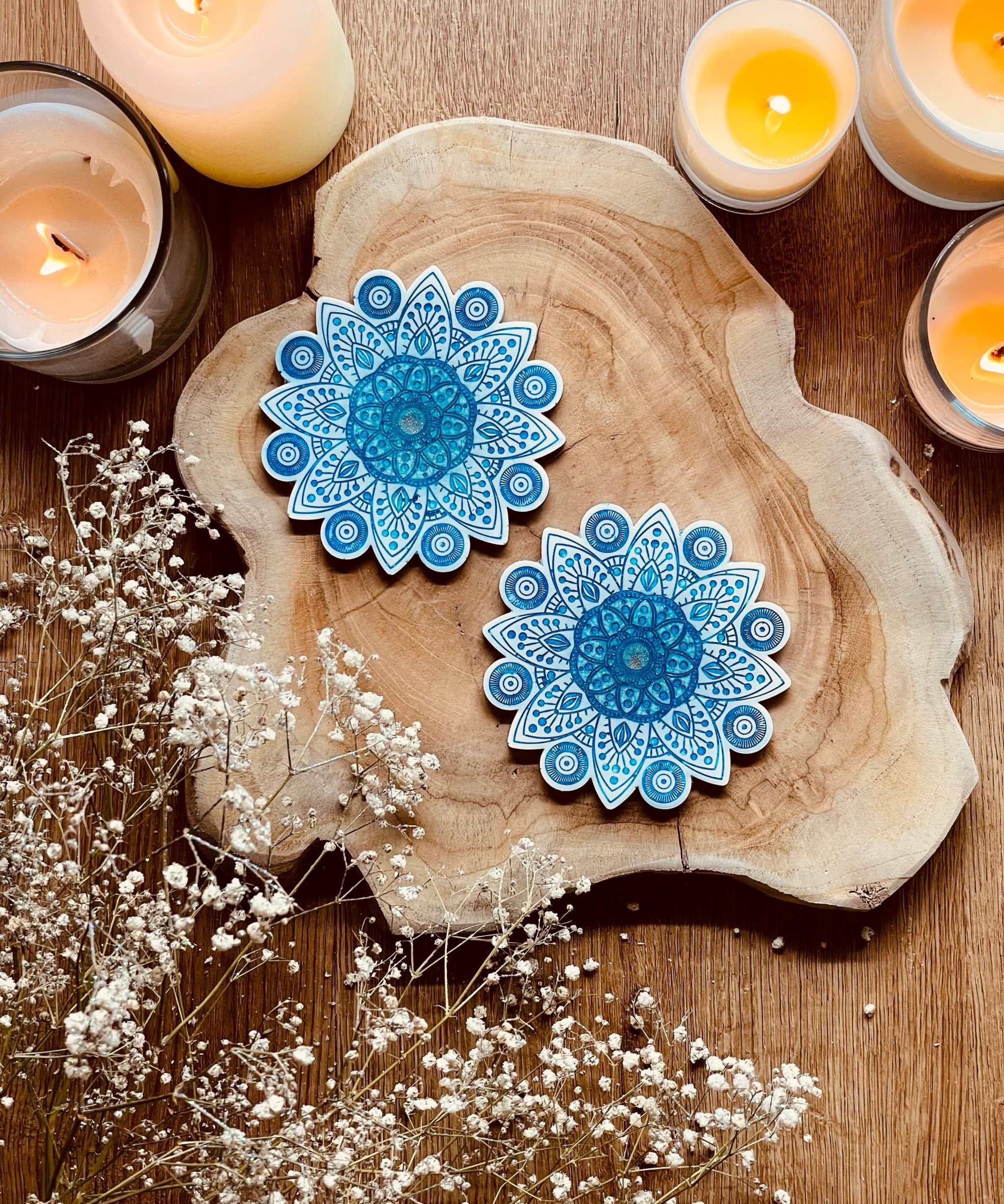 2 Mandala Untersetzer aus Resin in Weiss mit blauen Details auf Holzplatte mit Kerzen und Trockenblumen