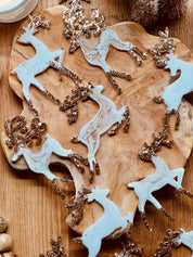Handmade white and gold resin reindeer Christmas tree ornaments on a wooden background.