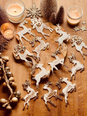 Weiße und goldene Rentier-Weihnachtsbaumanhänger aus Resin auf rustikalem Tisch.
