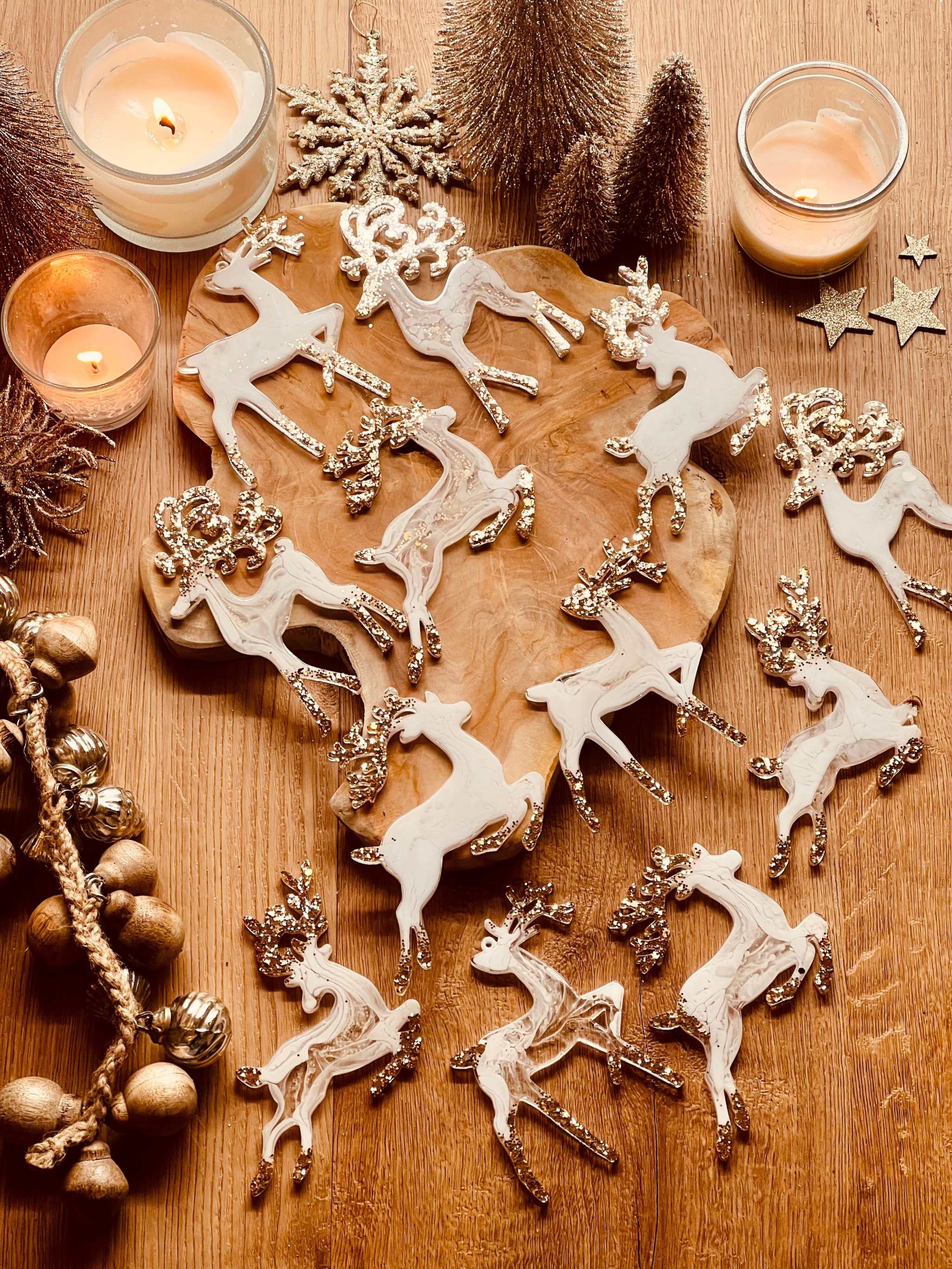 Weiße und goldene Rentier-Weihnachtsbaumanhänger aus Resin auf rustikalem Tisch.