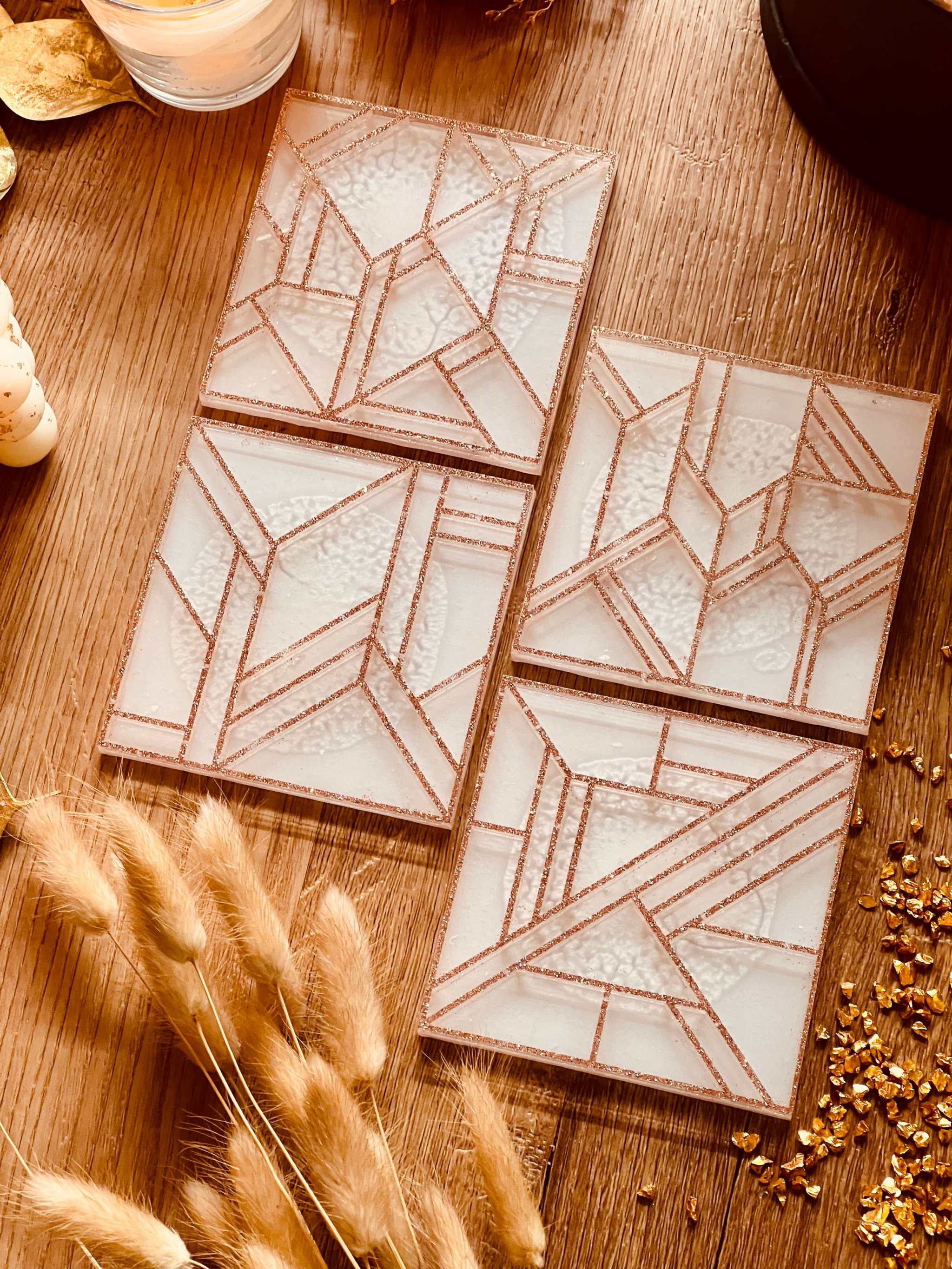 Set aus vier modernen weißen Untersetzern aus Resin mit goldfarbenem 3D-Design auf Holztisch