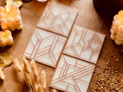 moderne Untersetzer aus Resin weiß mit goldenem 3D Design im 4er Set auf Holztisch mit Kerzen und Deko