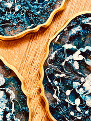 4 Untersetzer aus blauem Resin mit goldenen Details und wellenförmigem Rand auf Holztisch