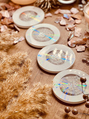 5 Untersetzer aus Resin in Weiss mit goldenen und holographischen Details auf Holztisch dekorativ angeordnet