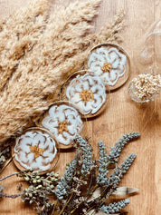 4 exklusive handgemachte weiße Resin Untersetzer mit goldenen Details im 4-teiligen Set auf Holztisch mit dekorativen Trockenblumen