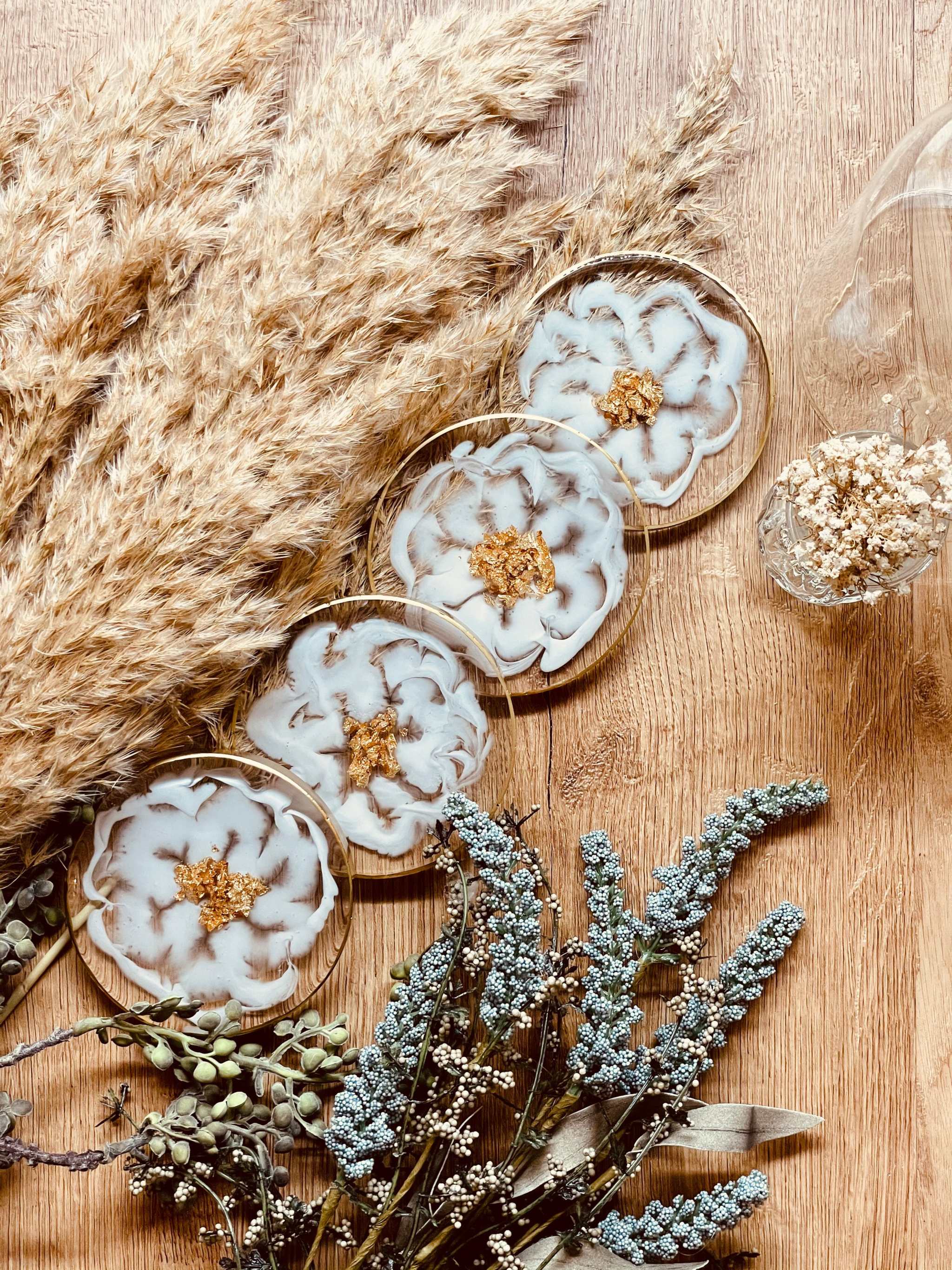 4 exklusive handgemachte weiße Resin Untersetzer mit goldenen Details im 4-teiligen Set auf Holztisch mit dekorativen Trockenblumen