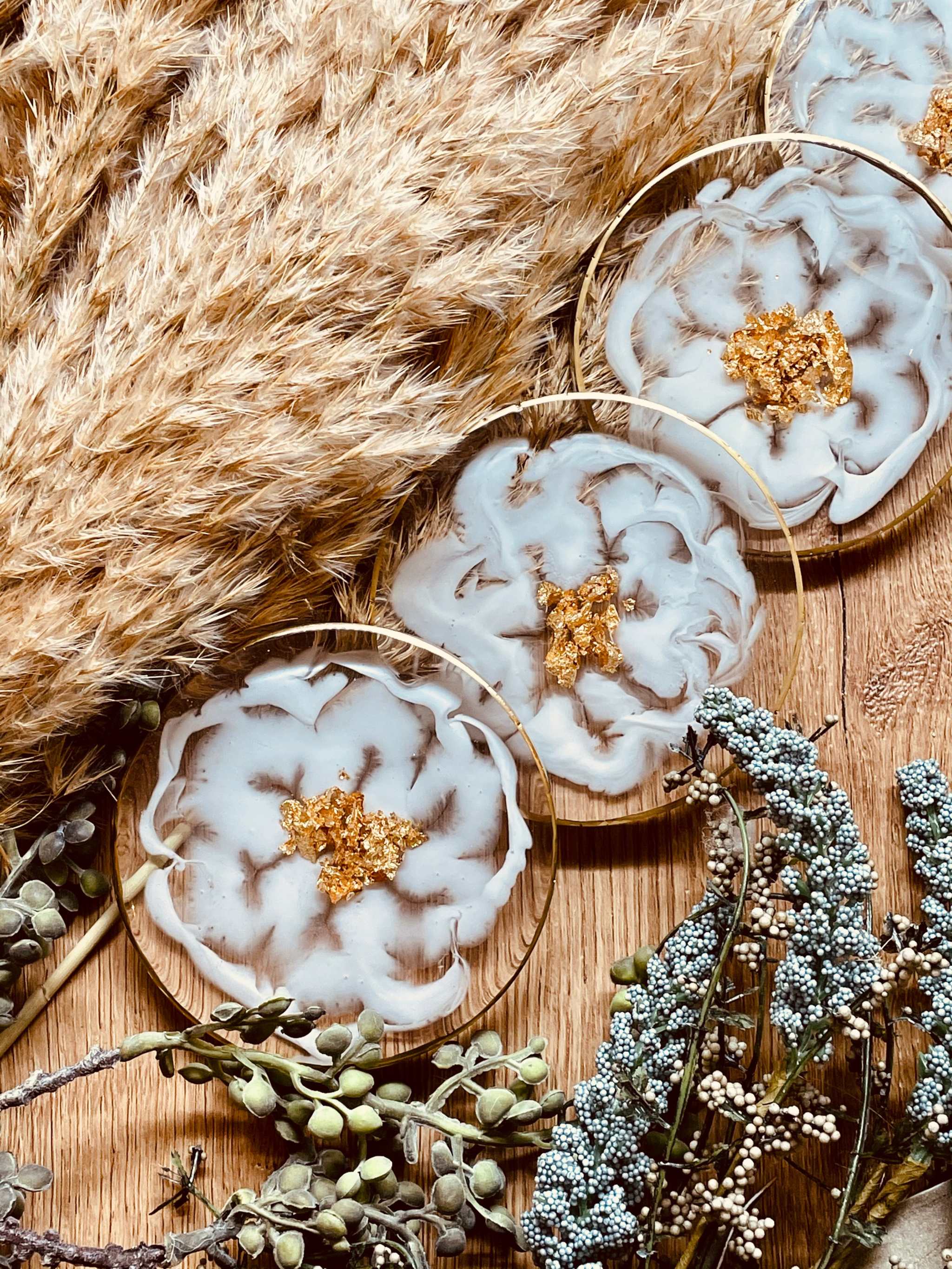 Vier exklusive handgemachte weiße Resin-Untersetzer mit goldenen Details und Blumenmuster auf Holzplatte