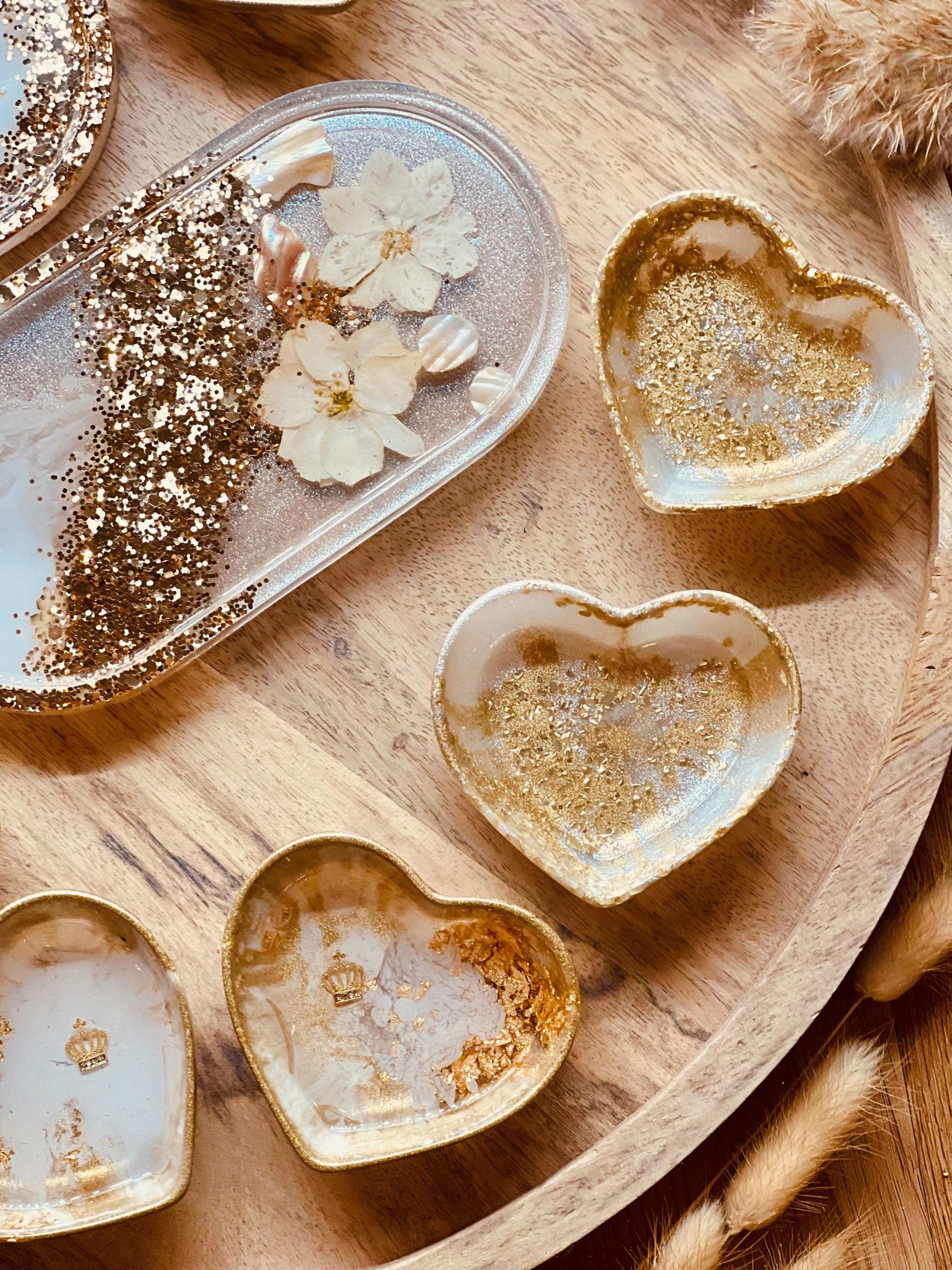 handgemachte weiße schmuckschalen aus resin mit goldperlmutt und blumen in herzform und oval auf holzplatte