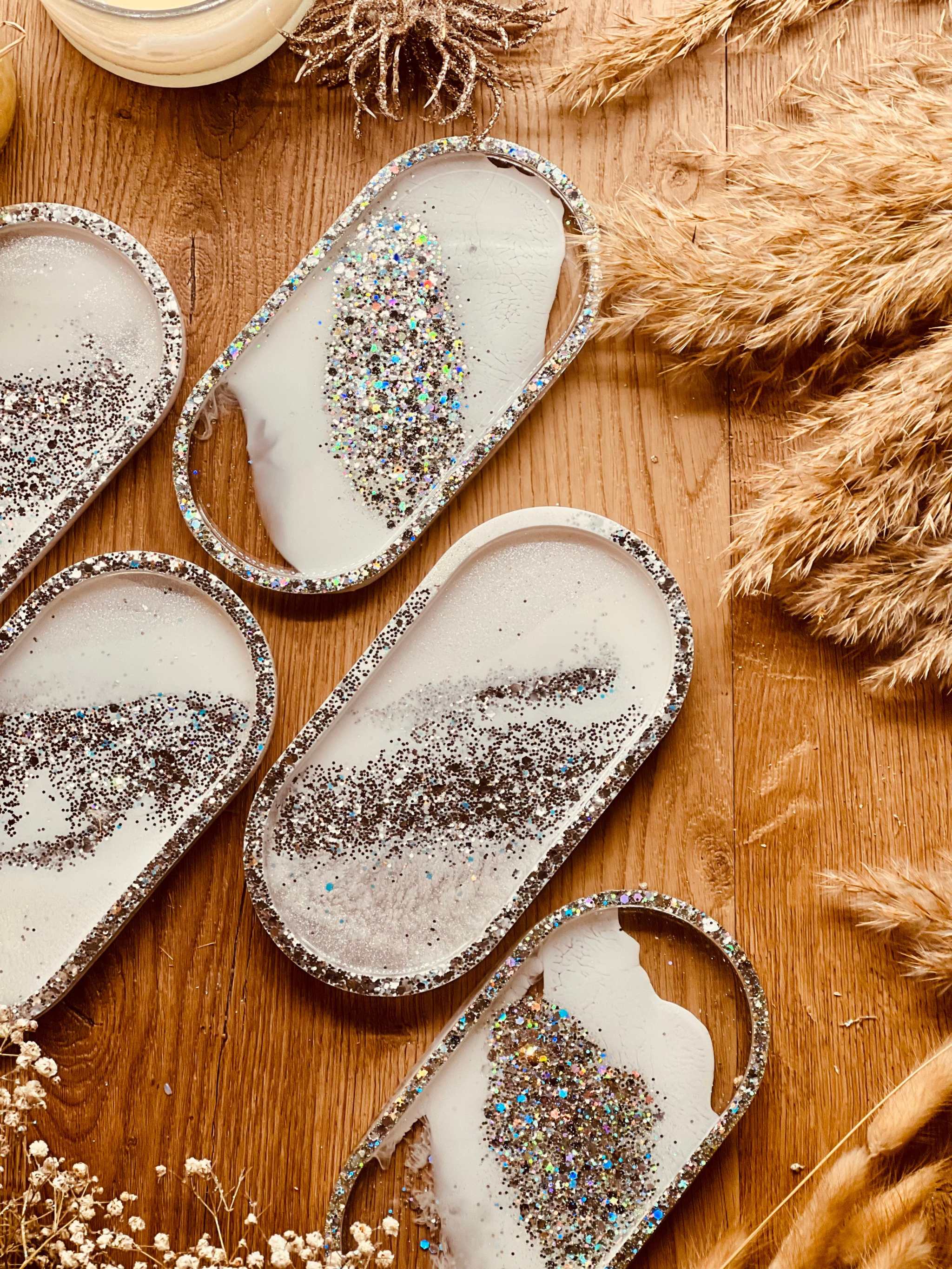 Handgemachte weiße Schmuckschalen aus Resin mit silbernen Glitzerdetails auf Holzuntergrund und Dekoration aus Trockenblumen