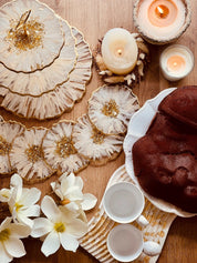 handgefertigtes Deko Set aus Epoxidharz mit weiß-goldenem 3D-Design bestehend aus Etagere, Schalen, Untersetzern und Tabletts auf Holztisch mit Kerzen und Blumen